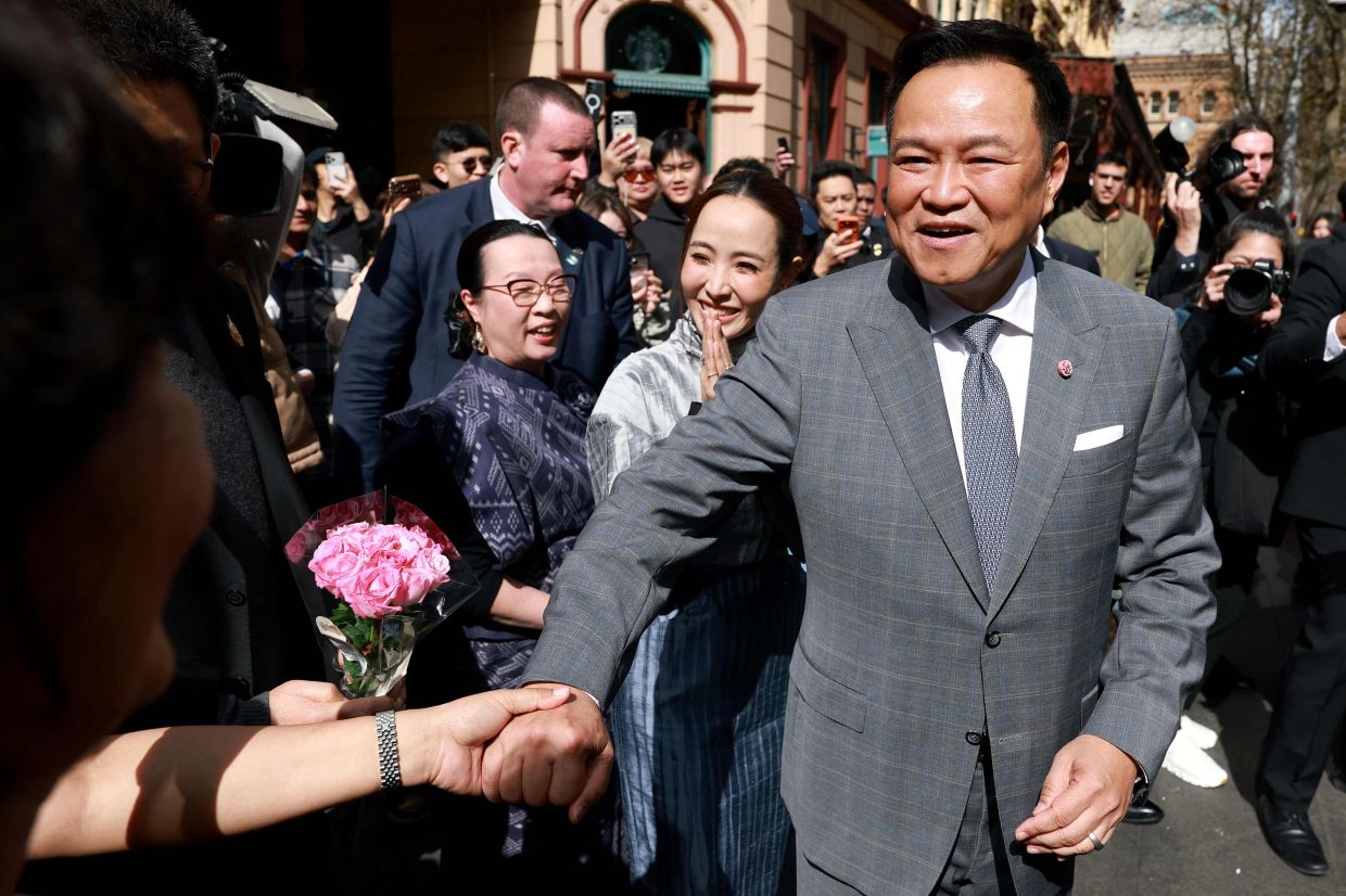 Thailand's Prime Minister Anutin Charnvirakul (right) meets a member of the public as his wife, Thananon Niramit (centre), reacts during a visit to Thaitown in Sydney on August 18, 2026. The Thai Prime Minister is on a three-day official visit to Australia. -- Photo by DAVID GRAY / AFP