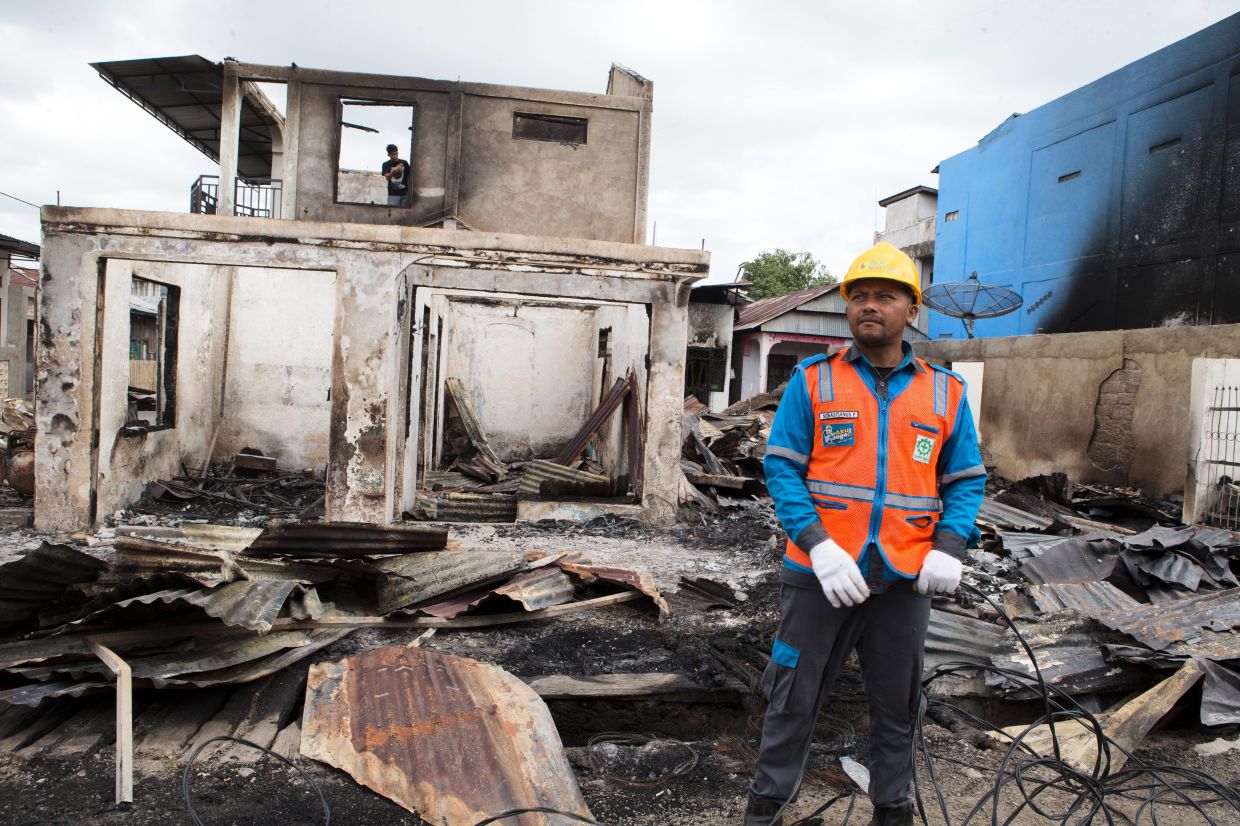 A worker reinstalling a power cable near a house destroyed by fire during an earthquake in Reo, East Nusa Tenggara province, Indonesia, on Aug. 19, 2026. - AP