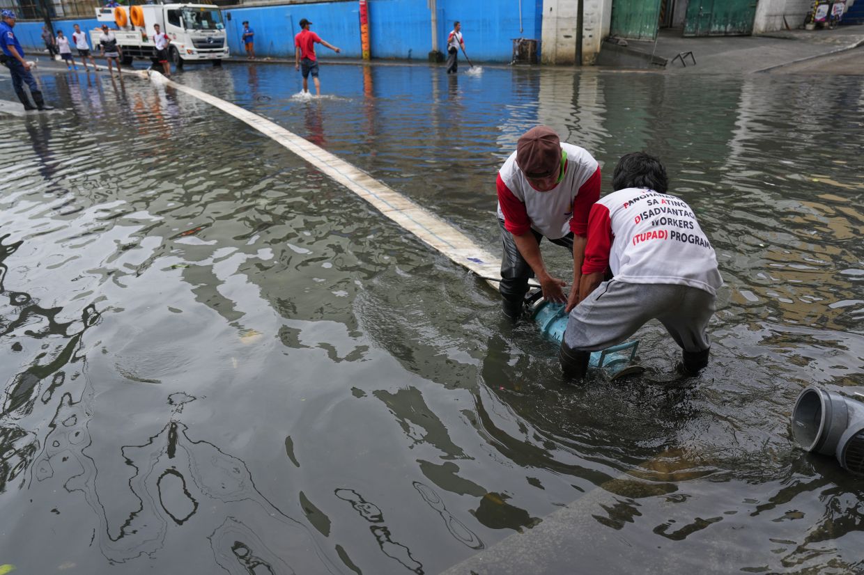 Workers using a pump to clear out flood waters caused by intense monsoon rains in Quezon City, Metro Manila, Philippines on Aug 19, 2026. - AP