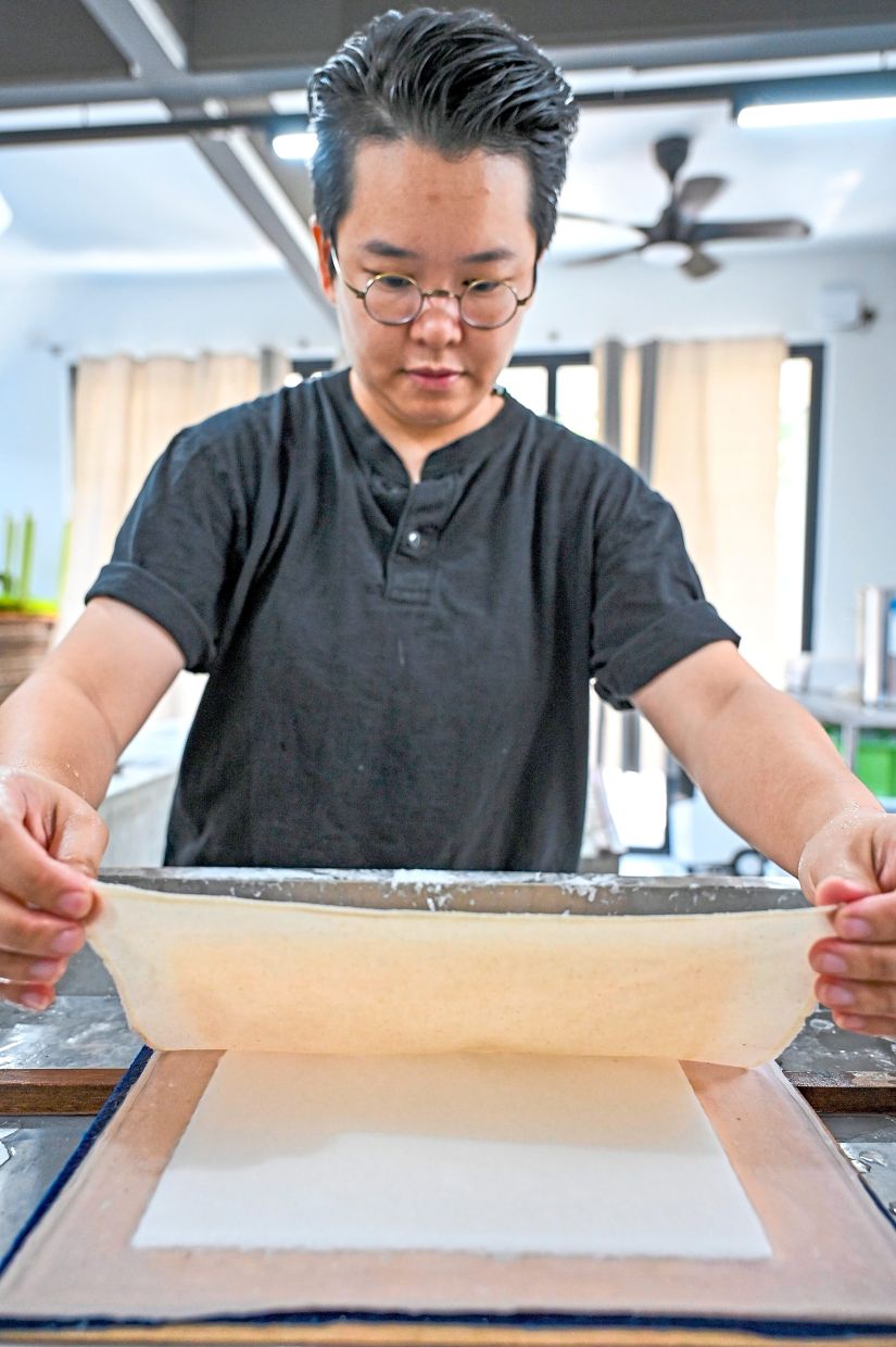 Soo places a piece of cloth over the deckle before lifting the handmade paper.