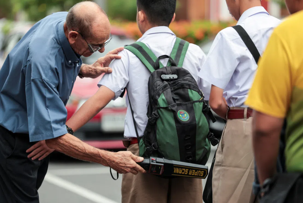 A teacher using a metal detector to screen for weapons and checks students' bags as they enter a school in Bangkok on Aug 10, following a deadly shooting at Debsirin Nonthaburi School - Reuters