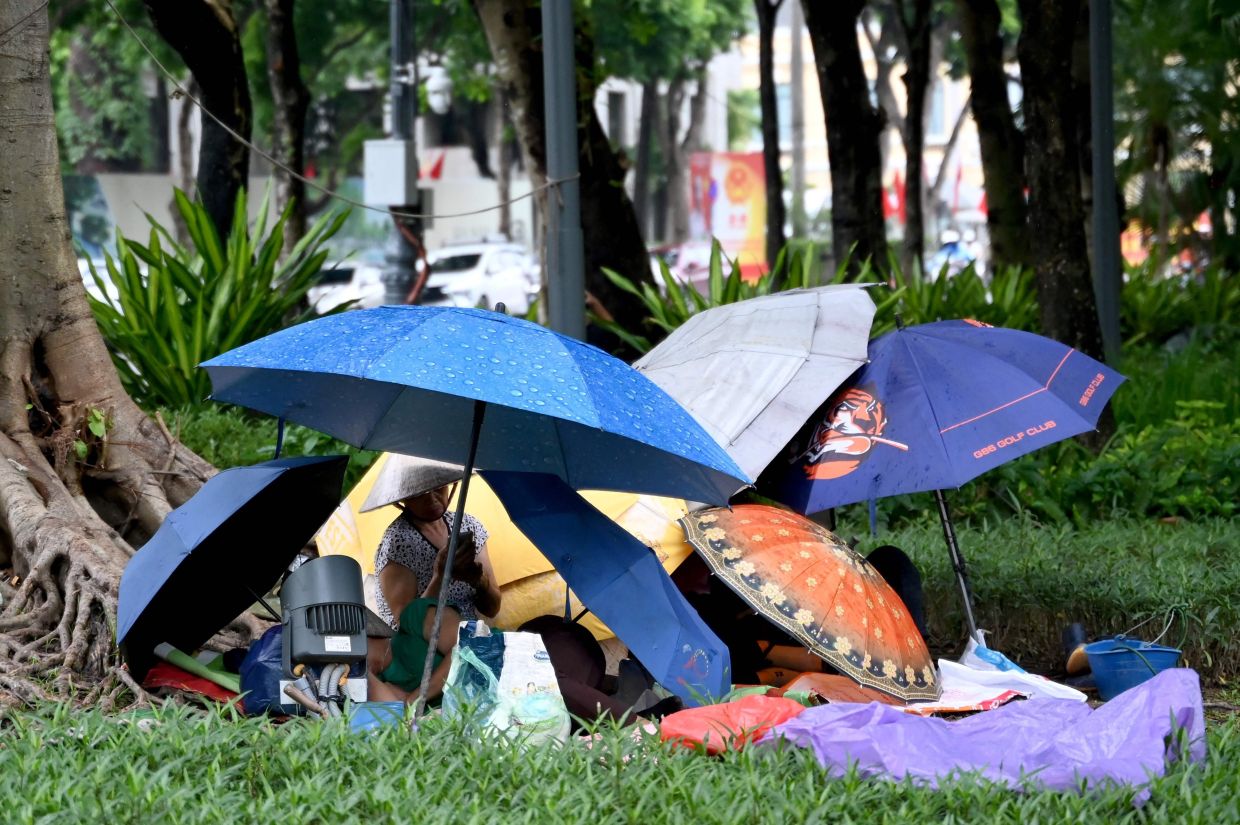A group of women uses umbrellas to shield themselves from the rain while resting in a flower garden in Hanoi.-- Photo by Nhac NGUYEN / AFP