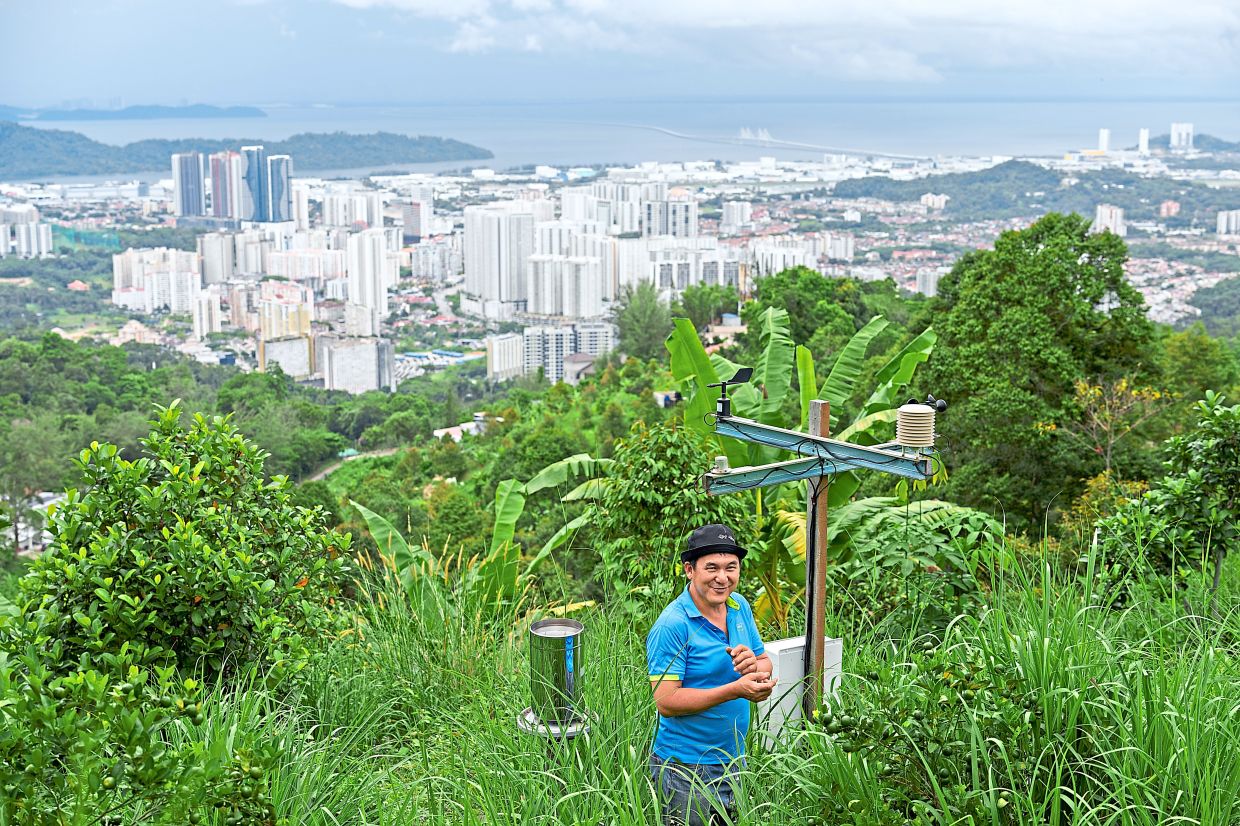 Kie stands beside a weather and climate sensor station overlooking Penang island in Balik Pulau.