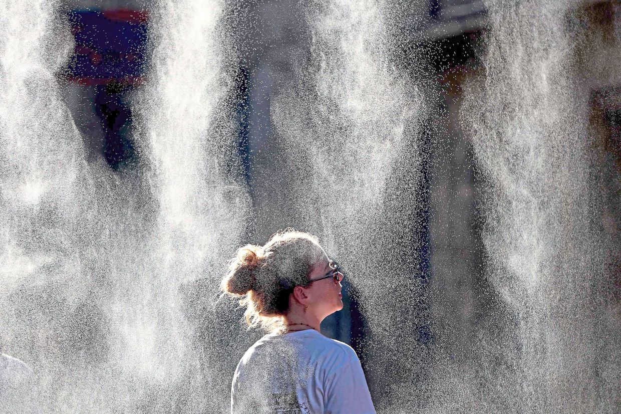 A woman cools off under a mist sprayer during an annual street music festival in Bordeaux, southwestern France. — ROMAIN PERROCHEAU/AFP