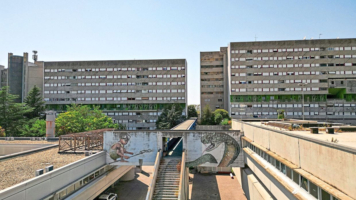 A drone view shows a mural-covered walkway, staircase and residential blocks at Corviale.