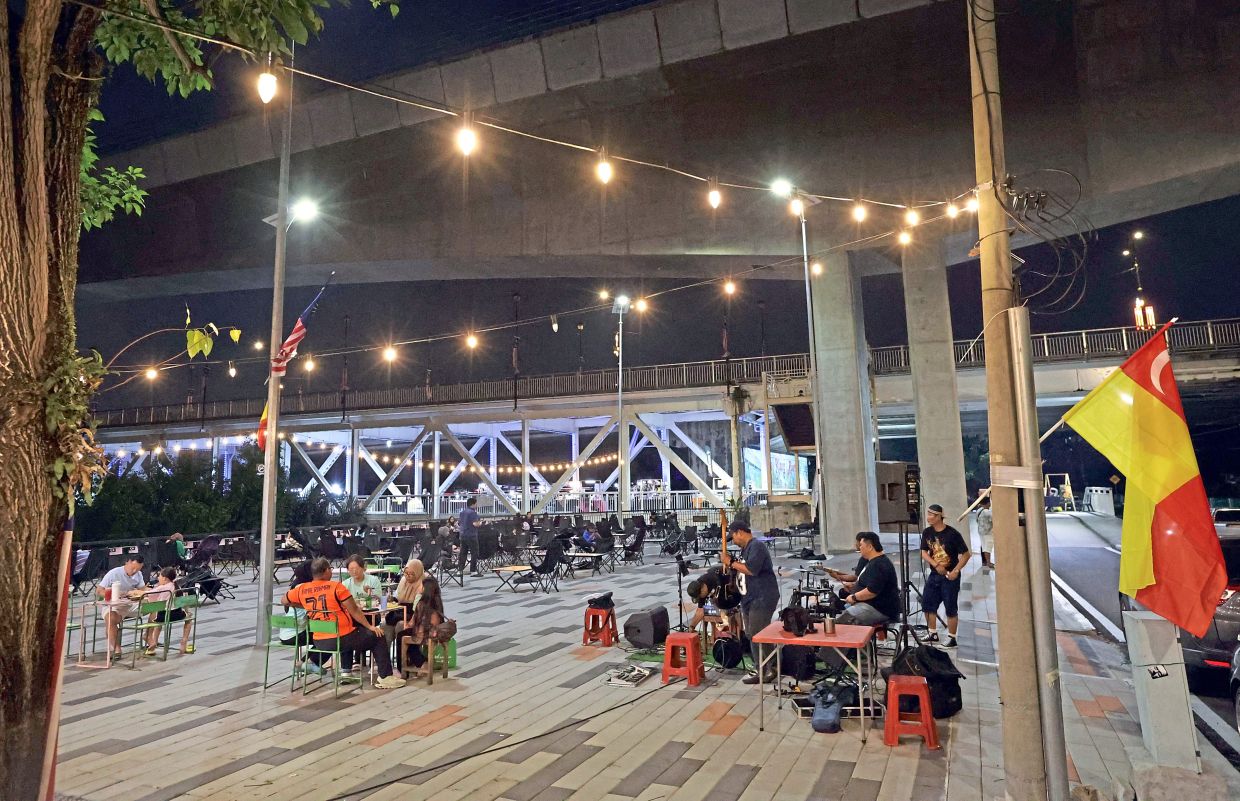 People enjoying food and drinks from surrounding stalls while listening to buskers just outside of Jambatan Kota.