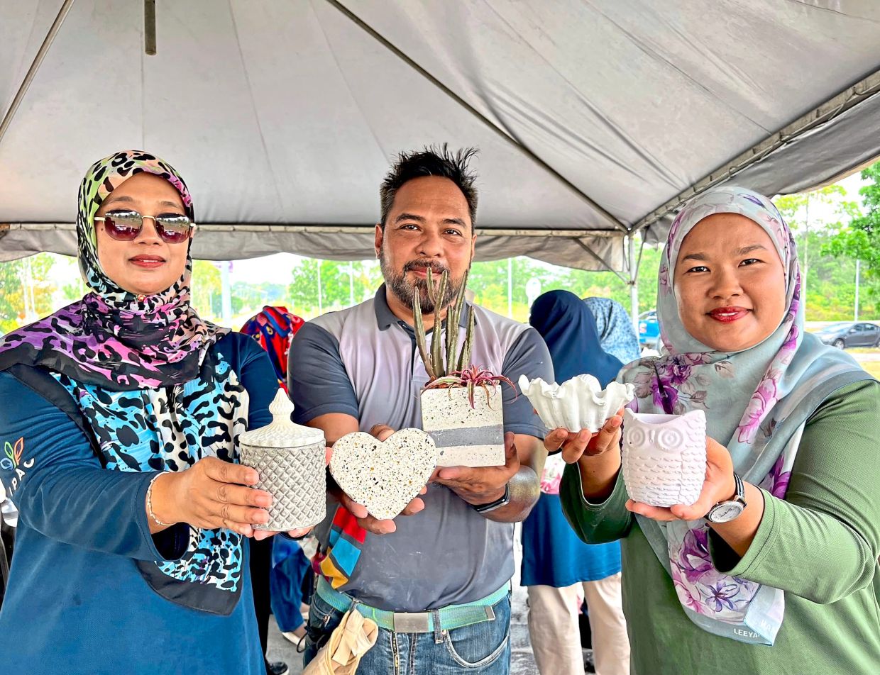 Faisal (centre) flanked by Iskandar Puteri Agriculturalist Community members Masayu Muhamad (right) and Ruhaidah Mohd Aris showing the finished products made from recycled glass crushed into powder.