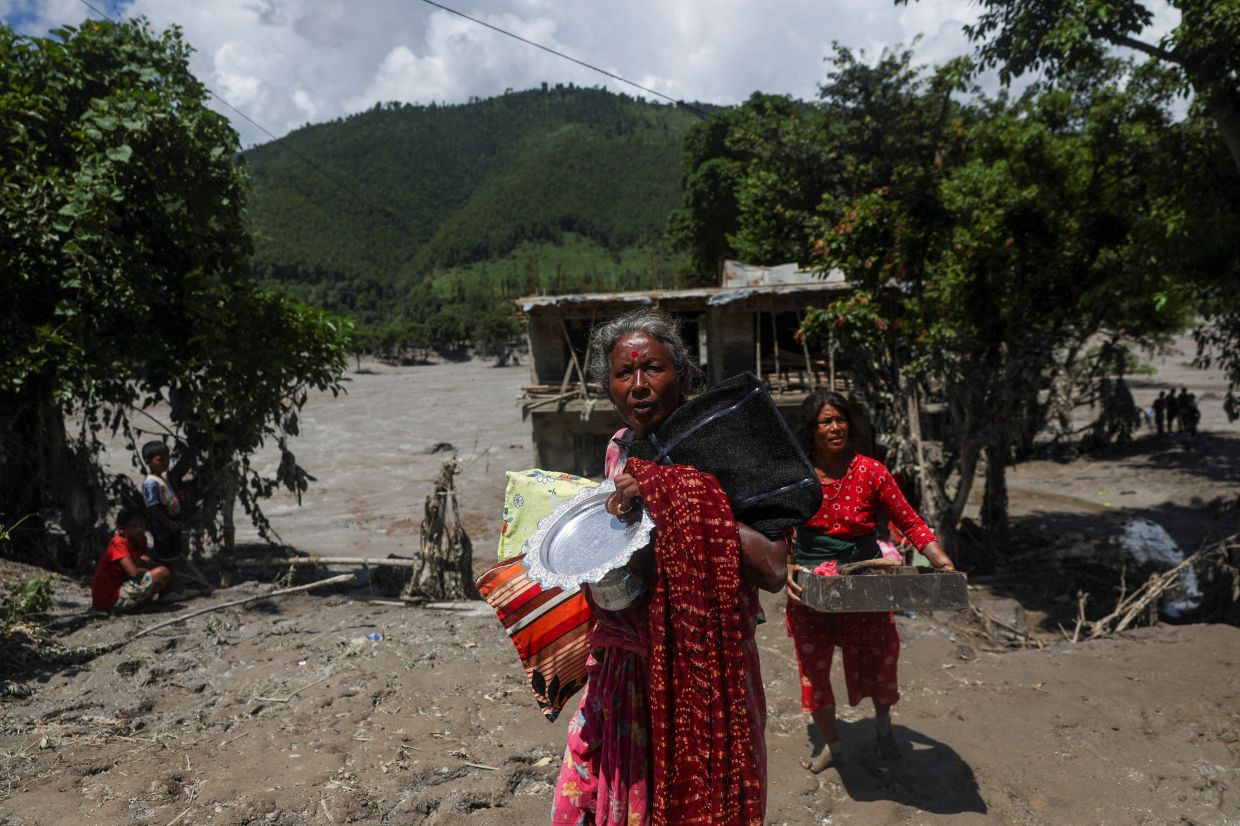 Women carry belongings from their damaged homes after a flash flood and a mudslide, in Galchhi, Nepal, August 27, 2026. - Photo: Reuters