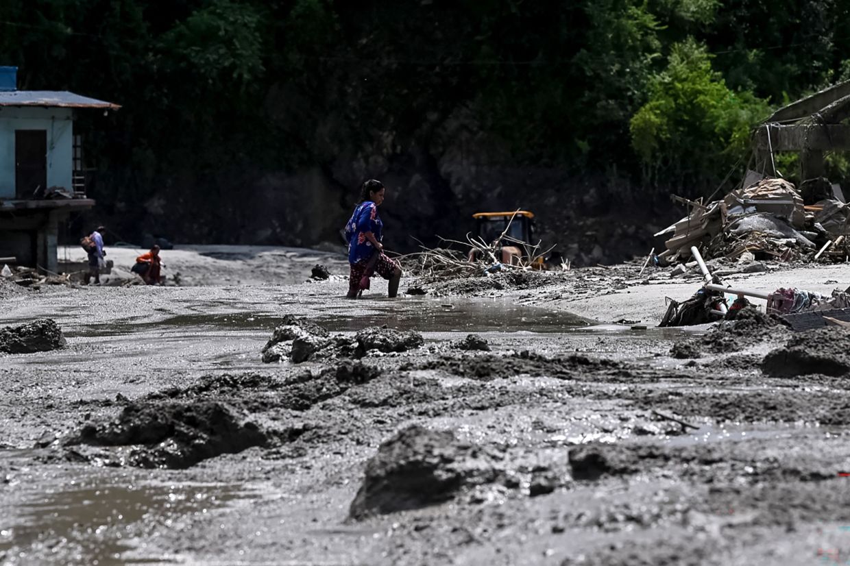 A woman wades along a road submerged in sludge and debris after flash floods in the Devighat area in Nepal's Nuwakot district on August 27, 2026. - Photo: AFP