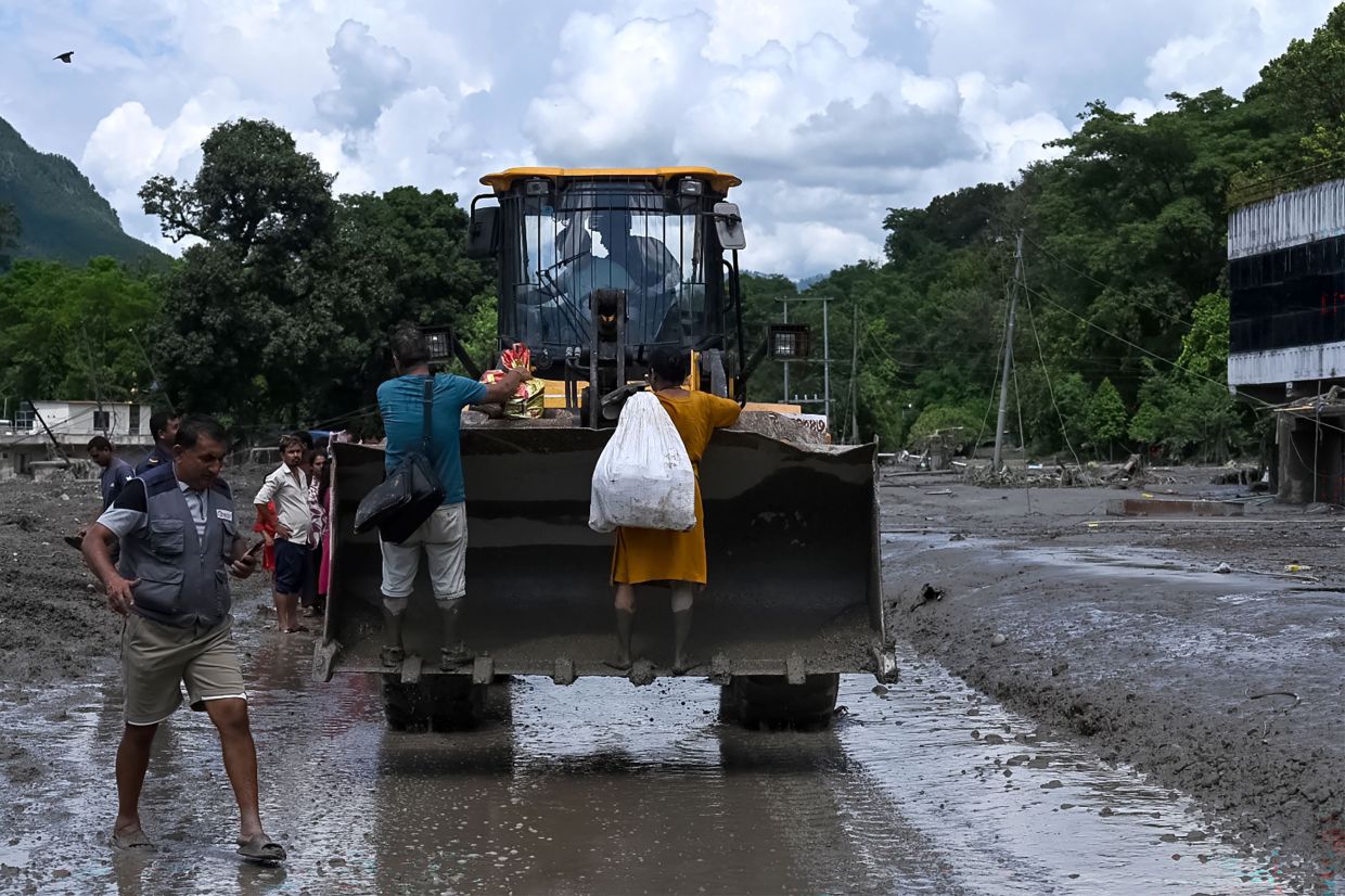Rescue personnel transport stranded residents using a bulldozer after flash floods in the Devighat area in Nepal's Nuwakot district on August 27, 2026. Rescue teams rushed on August 27 to find more than 1,300 people missing on the Nepal-Tibet border in flash floods and landslides that killed at least 165 and swept away entire villages. (Photo by Prakash MATHEMA / AFP)