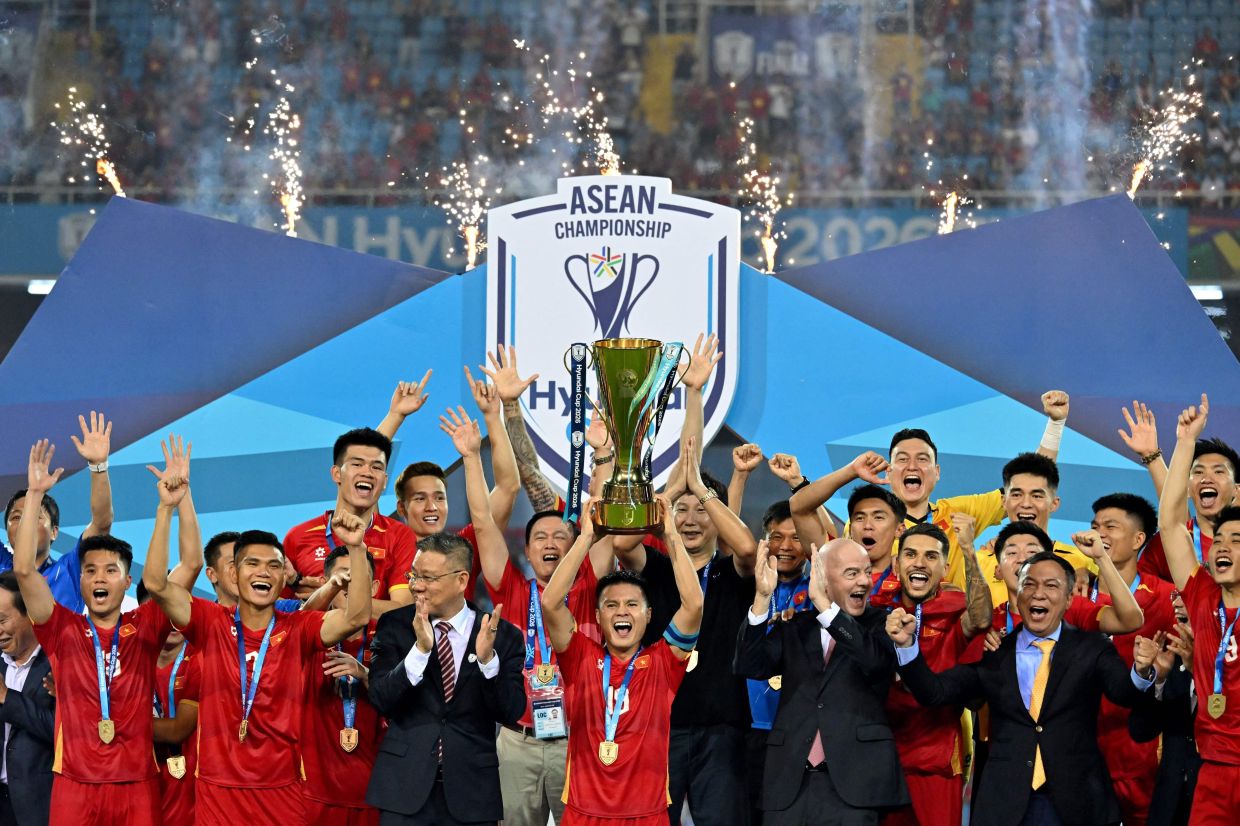 Vietnam's Captain Nguyen Quang Hai (centre) lifts the winner's trophy alongside FIFA President Gianni Infantino (right) and teammates after winning the final against Thailand at the My Dinh National Stadium in Hanoi. -- Photo by Nhac NGUYEN / AFP