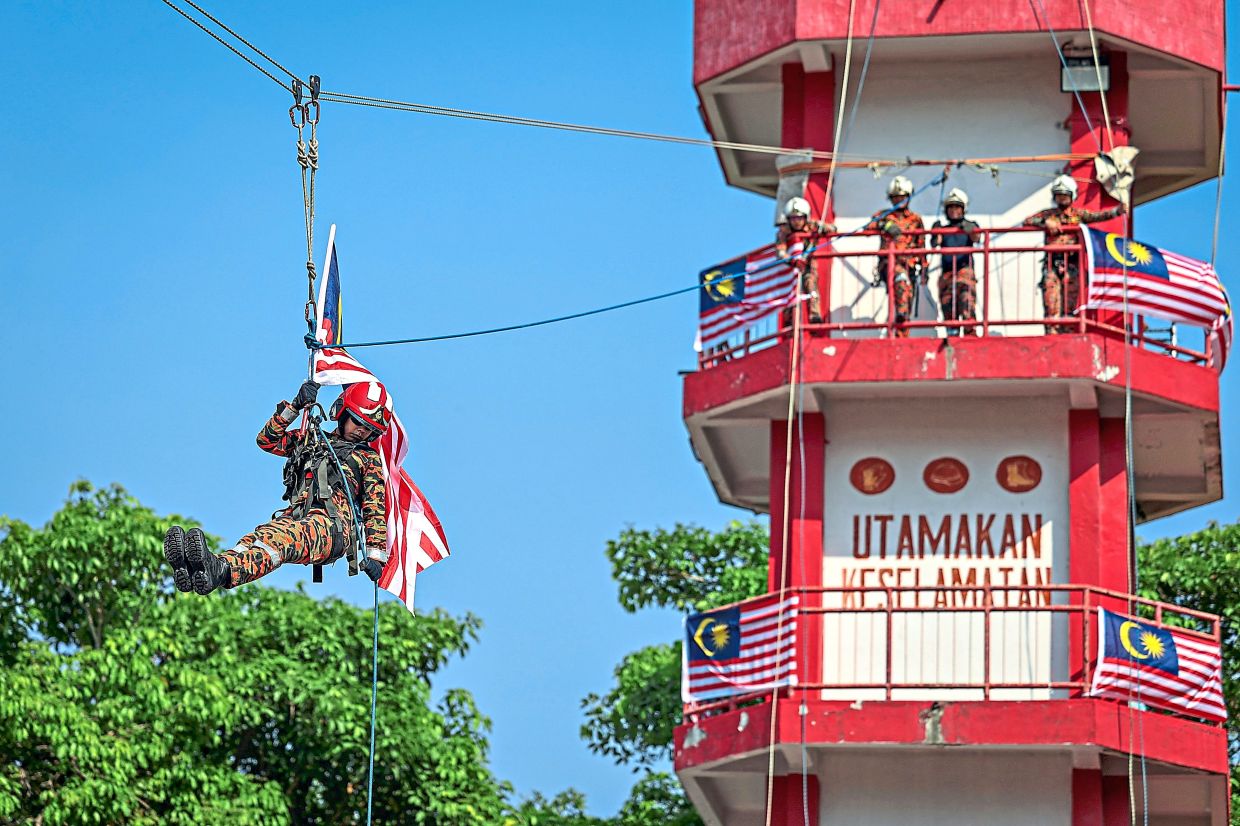 A Fire and Rescue Department personnel delivering the Jalur Gemilang via zipline as part of the Information Department’s National Day roadshow in Kuala Lumpur.