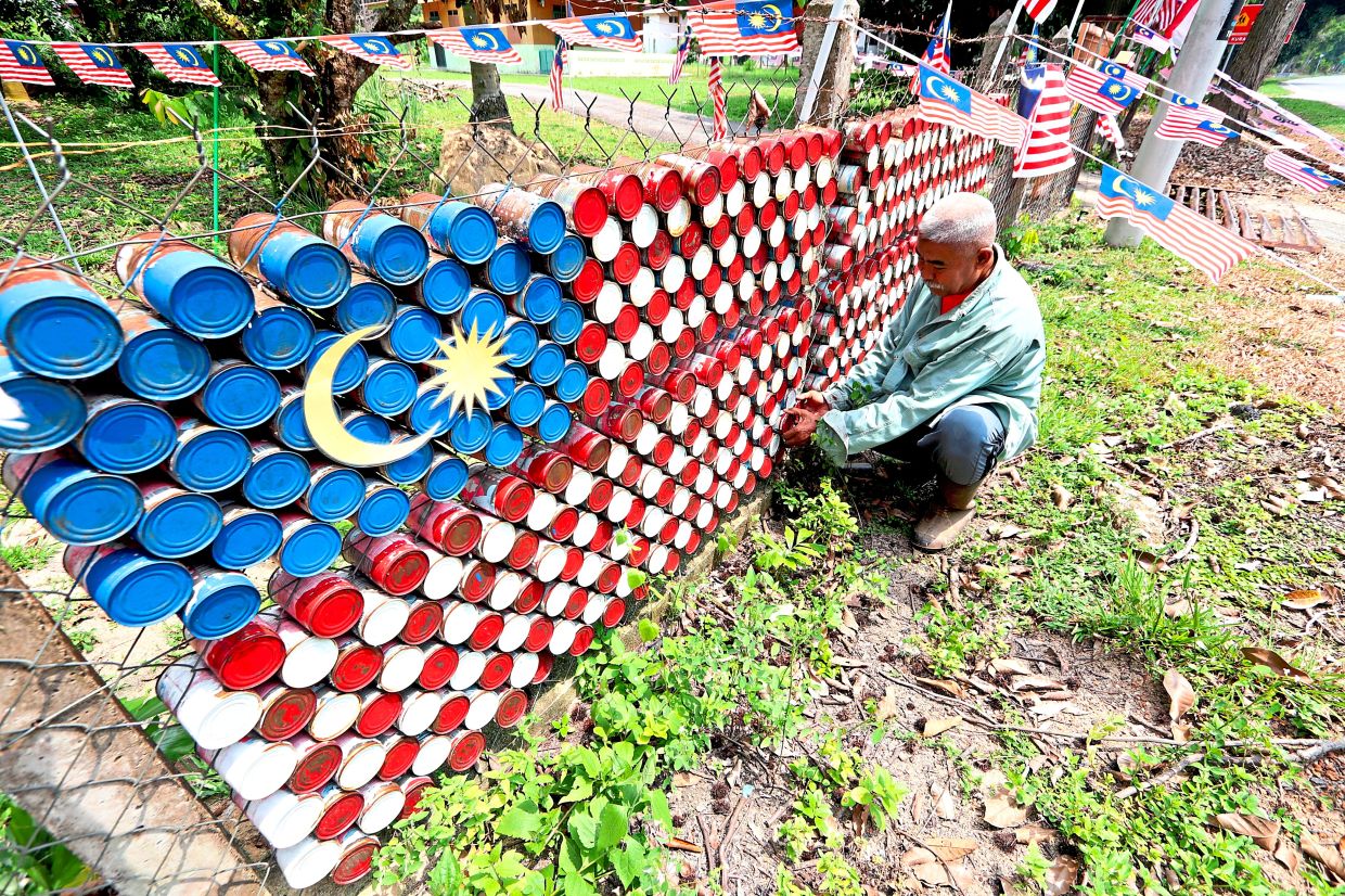 Azman Rejab, 62, putting the final touches on his Jalur Gemilang made using recycled cans at his home in Kampung Pulau Sebang, Melaka.