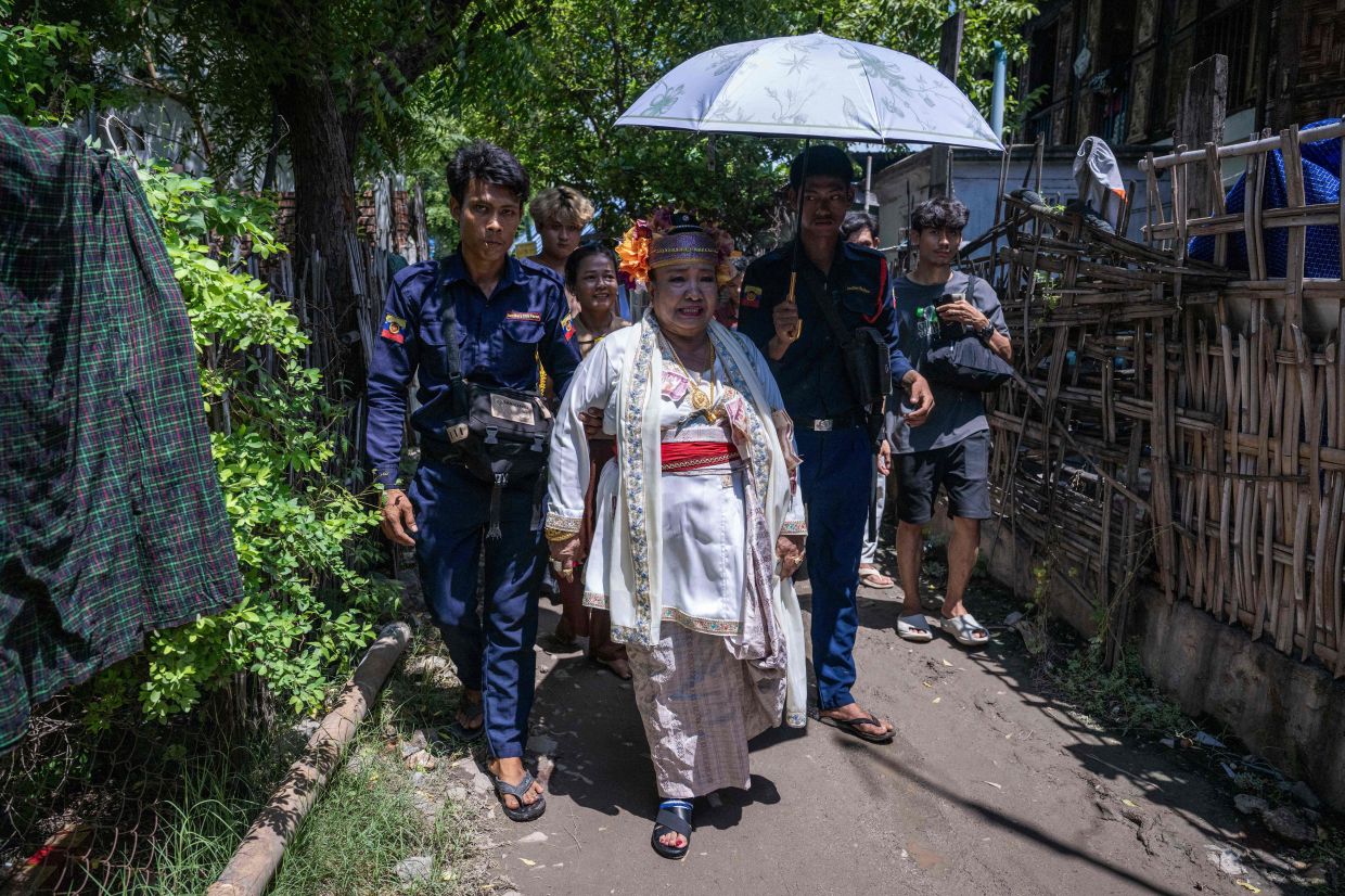 A spirit medium wearing a traditional floral headdress, walking along a street with devotees near the festival grounds. - AFP