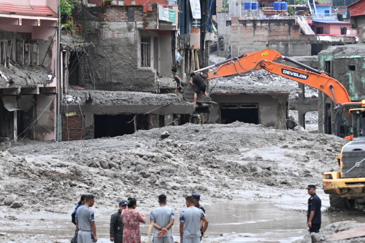 An excavator (top) helping people to collect some of their belongings from their house in the aftermath of flash floods at Trishuli. - AFP