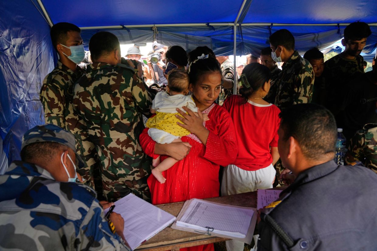 A woman and her child rescued from an area cut off by flash flooding stand for registration in Nepal's Nuwakot district on Saturday, Aug. 29, 2026. -- AP Photo/Dar Yasin