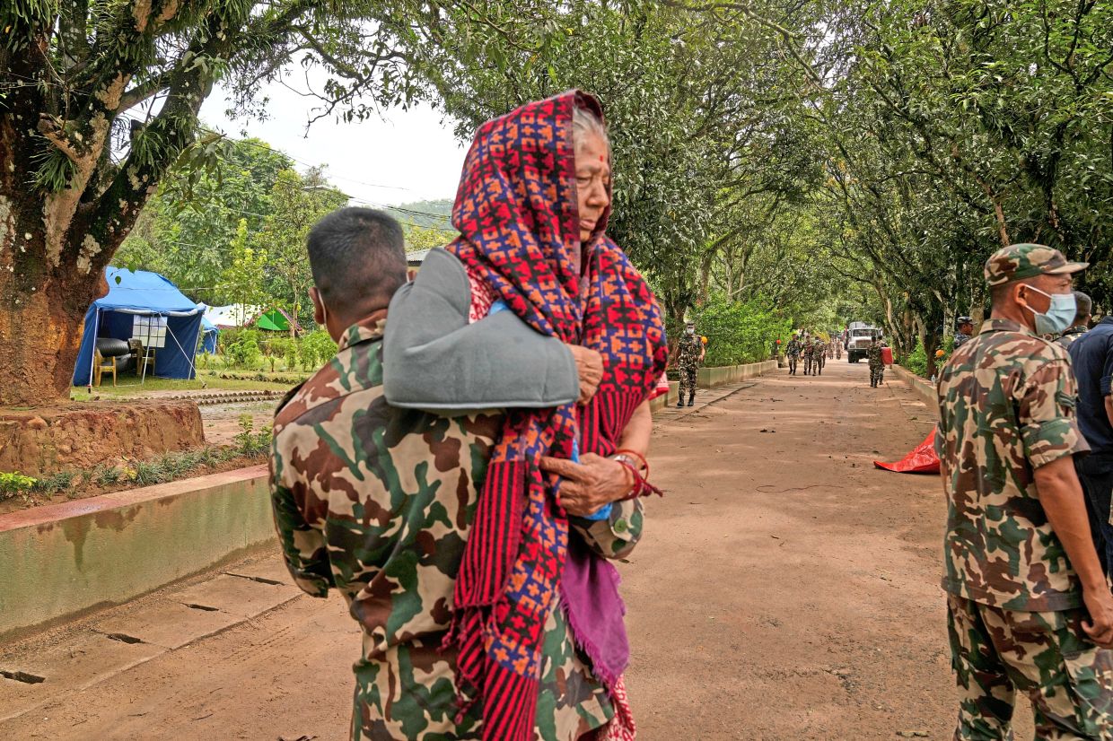 Angels in uniforms: A Nepalese soldier carrying an injured woman rescued from an area cut off by flash floods in Nuwakot. (Below) Soldiers unloading relief supplies for survivors in Nuwakot. — AP