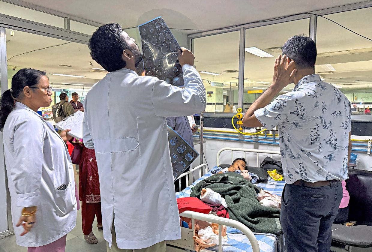 In good hands: A doctor examining a scan of Zoyal as he lies in a bed for treatment inside a hospital in Kathmandu. — Reuters 
