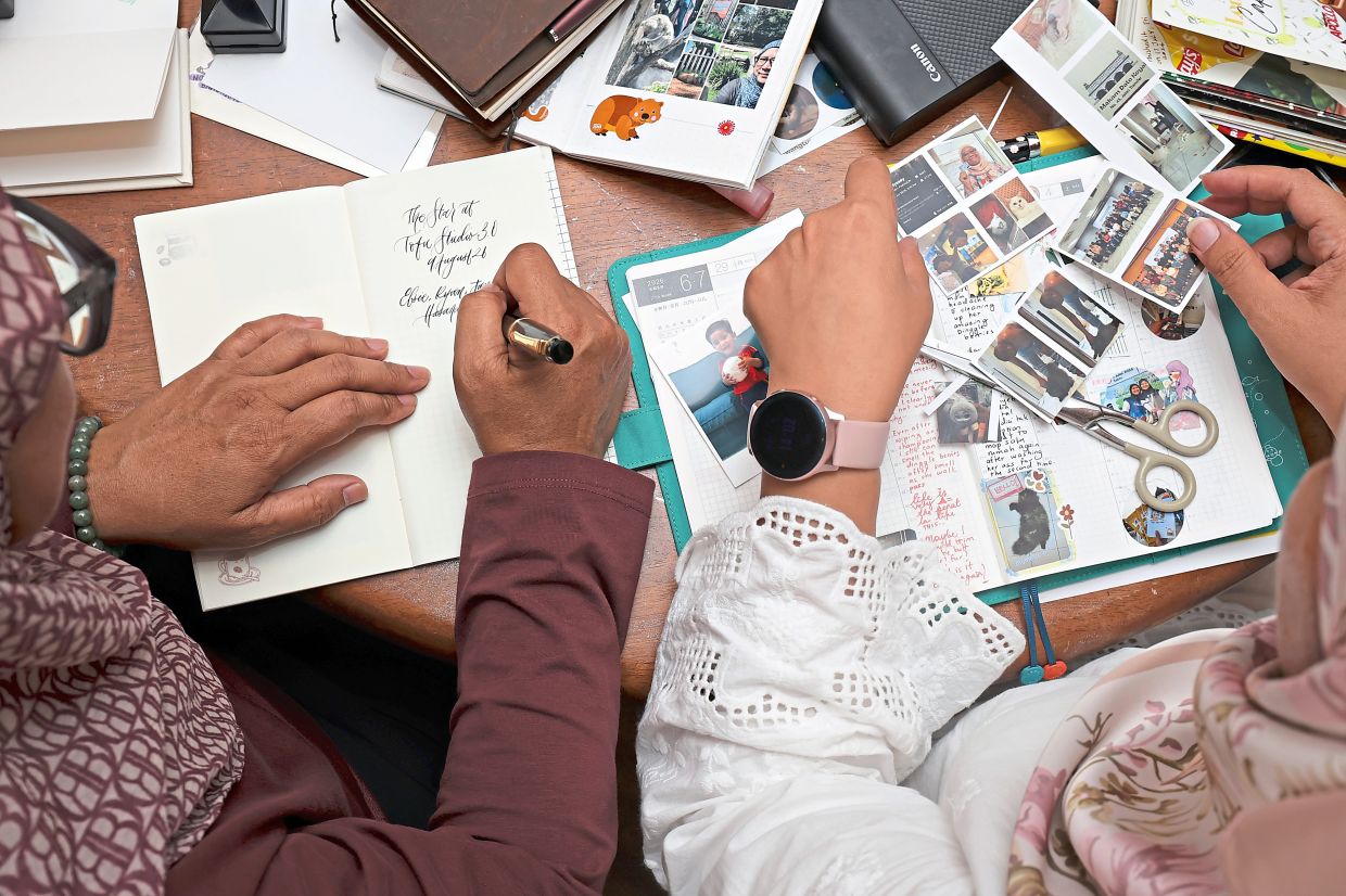 A participant using a fountain pen to write down her thoughts while another cuts and arranges miniature printed photographs to document her experiences.