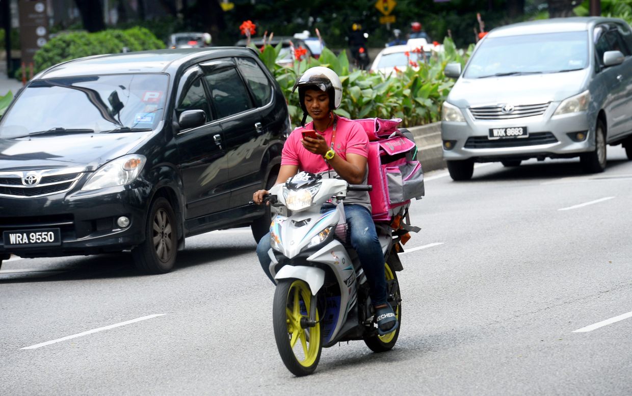 Here's a food delivery rider checking his messages on his mobile phone while on a motorbike, endangering his life and other road users. — Filepic