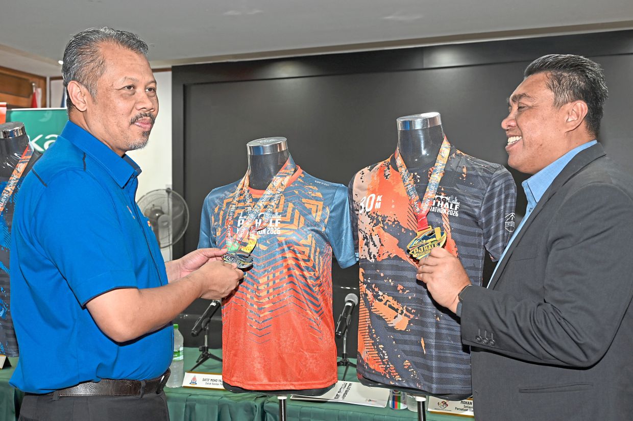 Mohd Yazid (left) and Ku Mustafa having a closer look at runners’ T-shirts and finishers’ medals for the half marathon. — Handout