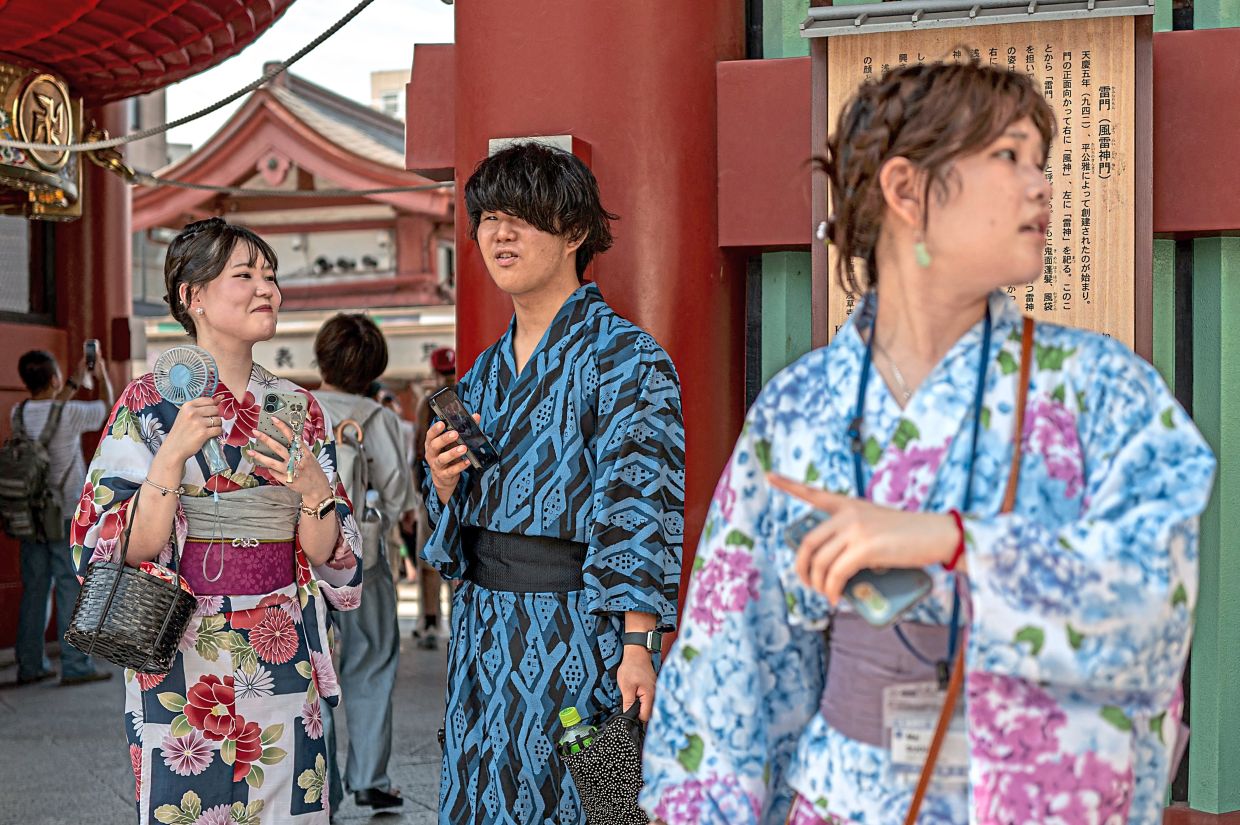 Cool relief: Hand-held fans are popular among Asians on hot days, like these tourists visiting the Sensoji Temple in Tokyo. — AFP