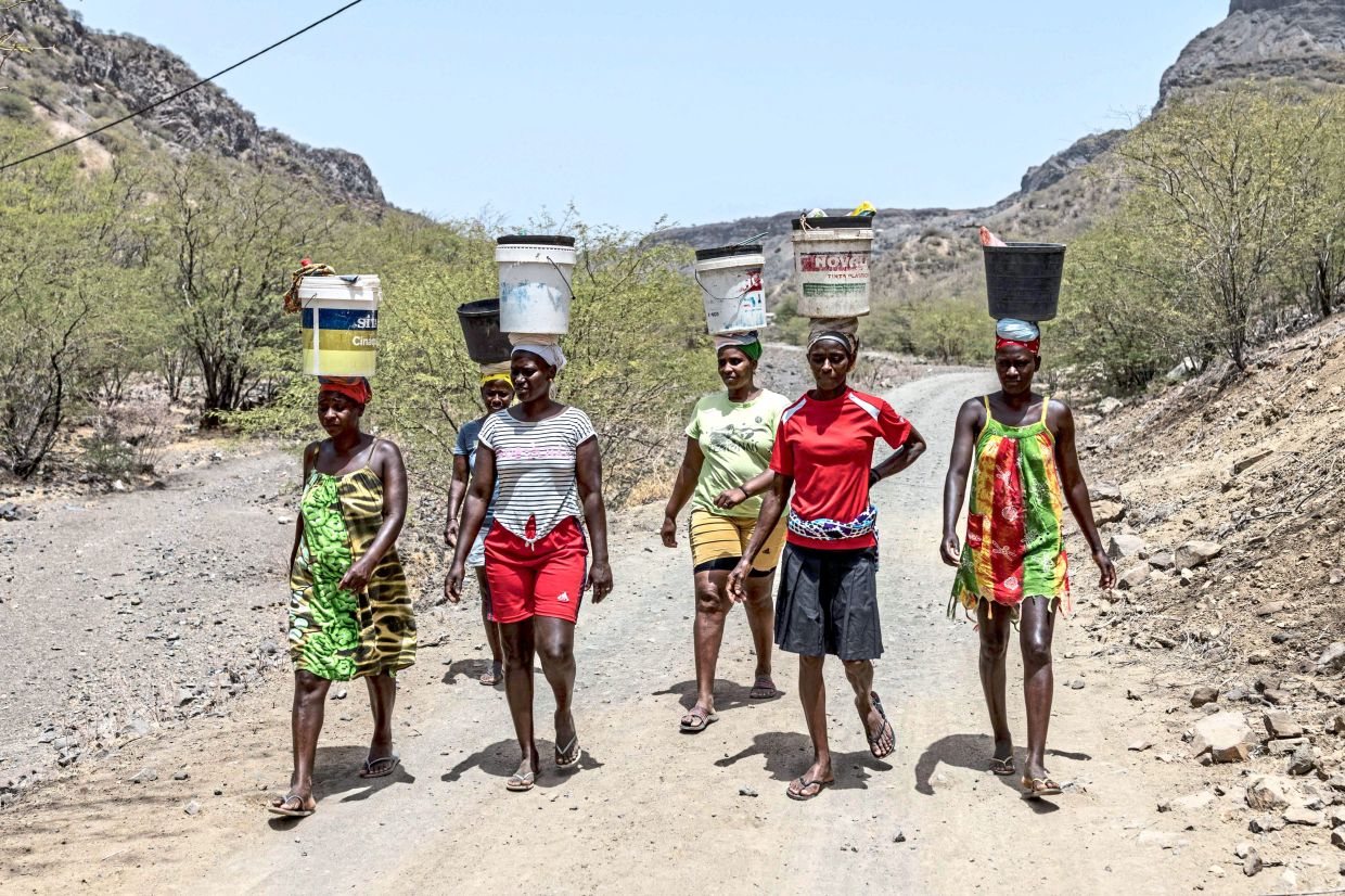 Women balance buckets on their heads as they walk to the beach to mine sand for commercial sale in Charco.