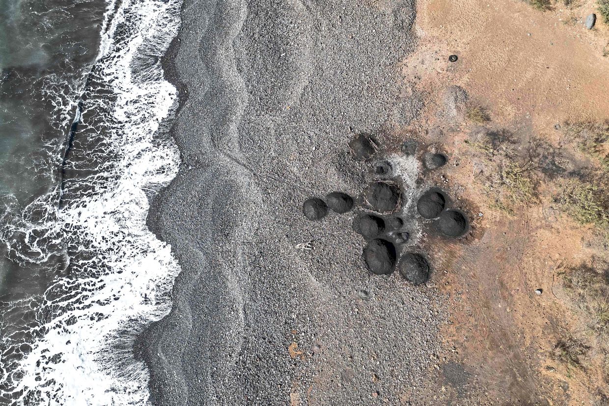 An aerial view of piles of black sand on a beach depleted by sand mining for commercial sale near Ribeira da Barca.
