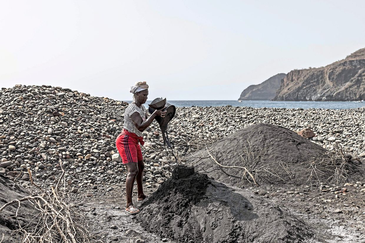 Tavares empties a bucket full of black sand on one of her piles at a beach.