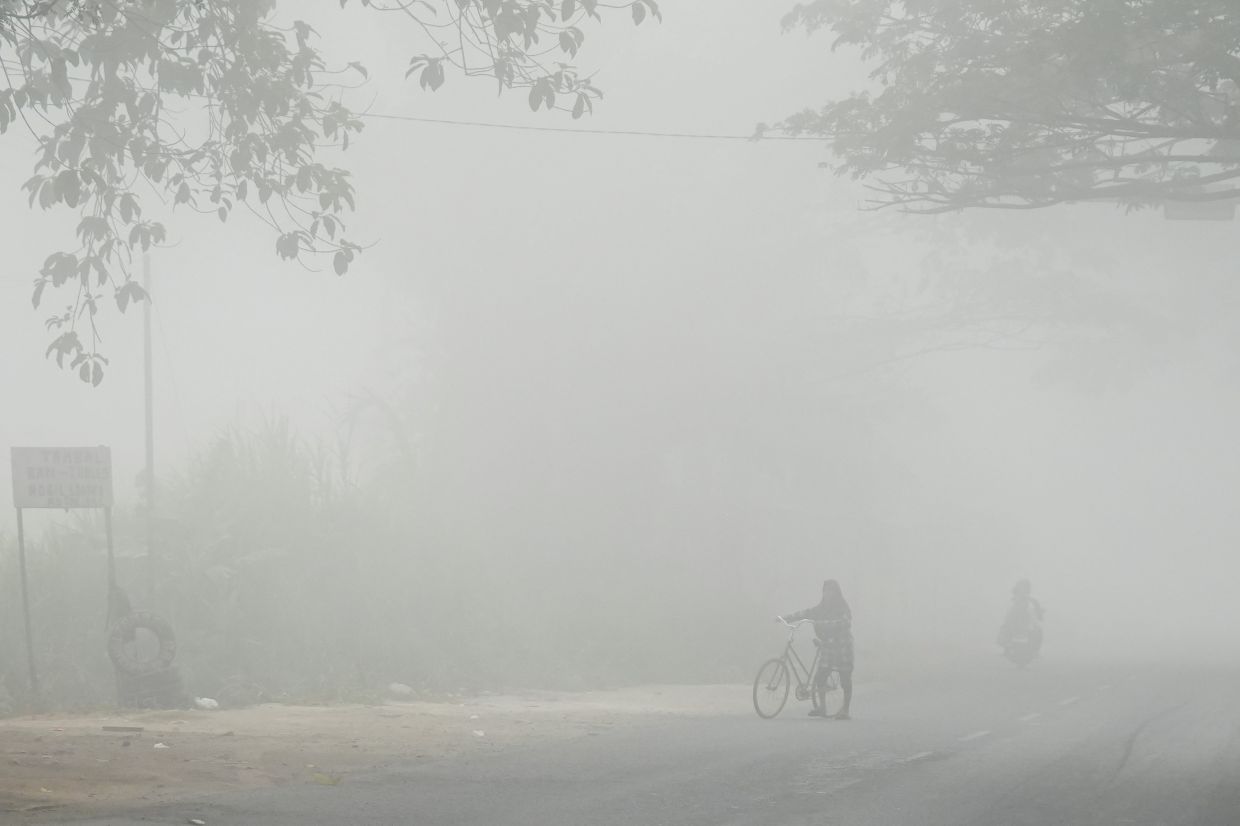 A person walks with a bicycle along a road shrouded in haze from wildfires in Banyuasin, South Sumatra province, Indonesia, on Sunday, September 6, 2026. -- Photo: REUTERS/Abriansyah Liberto