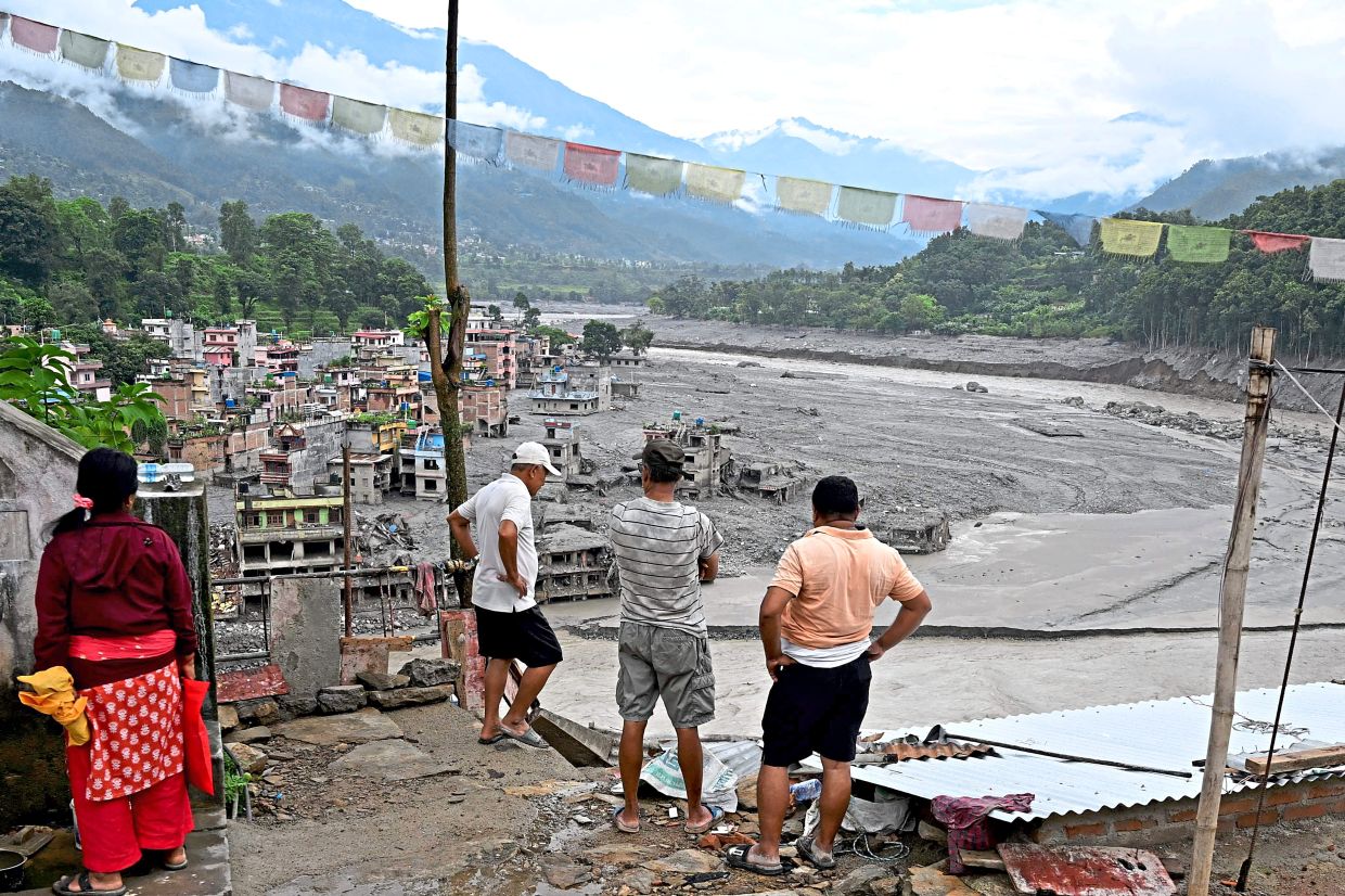 People looking at damaged buildings at Trishuli Centre, with the Himalayan range in the background. — AFP