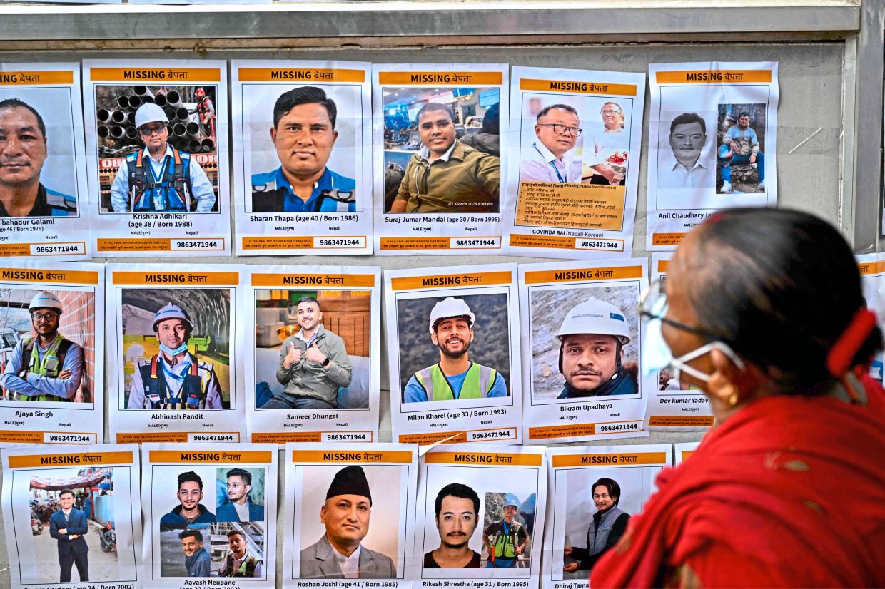 6. A woman looking at photographs of people missing after the flash floods, displayed outside a temporary relief camp in Trishuli. — AFP