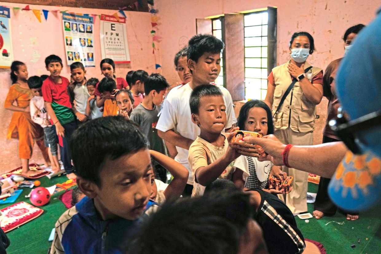 3. Volunteers distributing packets of biscuits to children displaced by recent flash floods inside a classroom at a school converted into a temporary shelter in Nuwakot district. — AP
