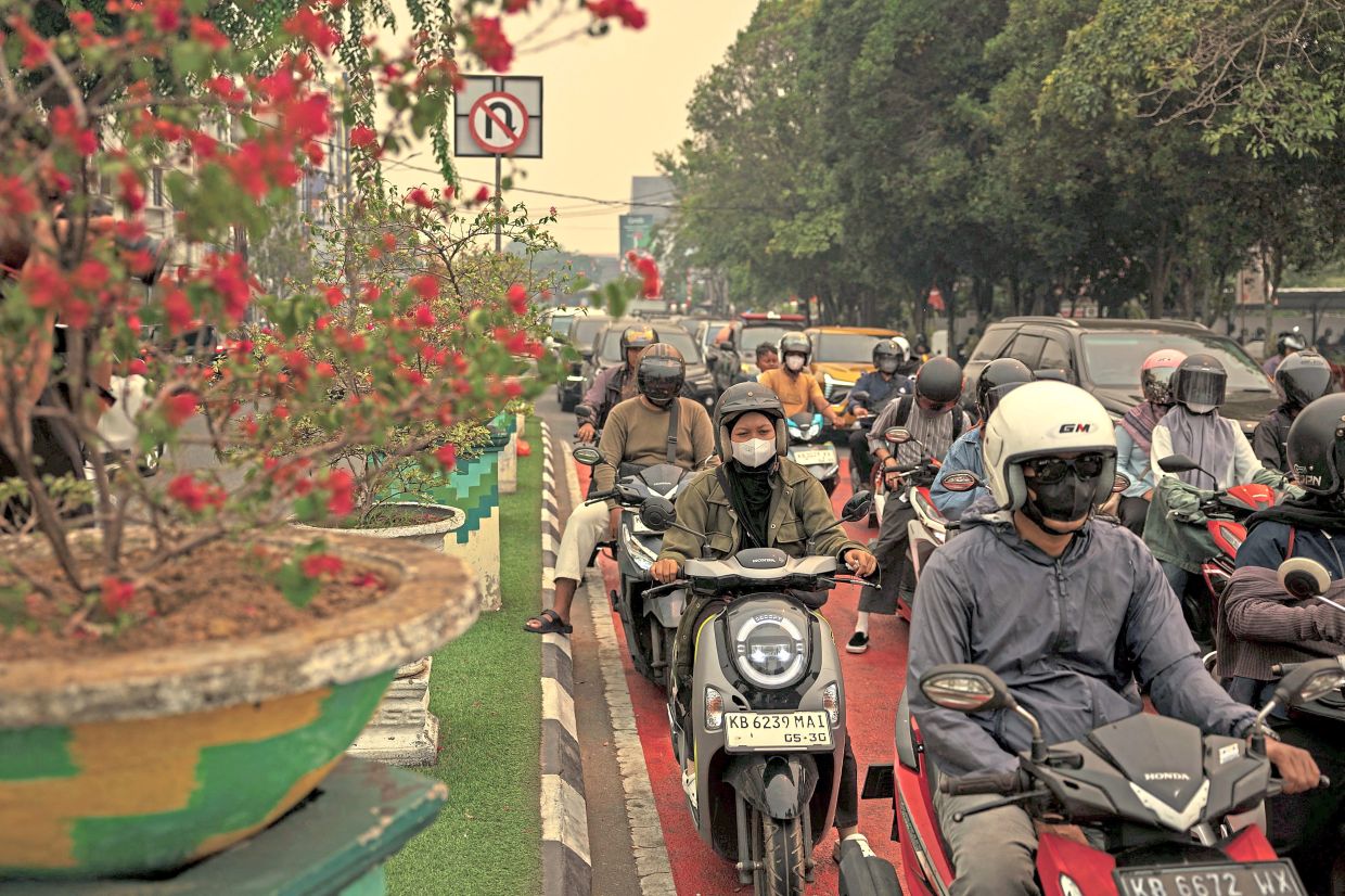 Motorists wearing protective masks wait at an intersection as wildfire haze blankets Pontianak, West Kalimantan. — Reuters