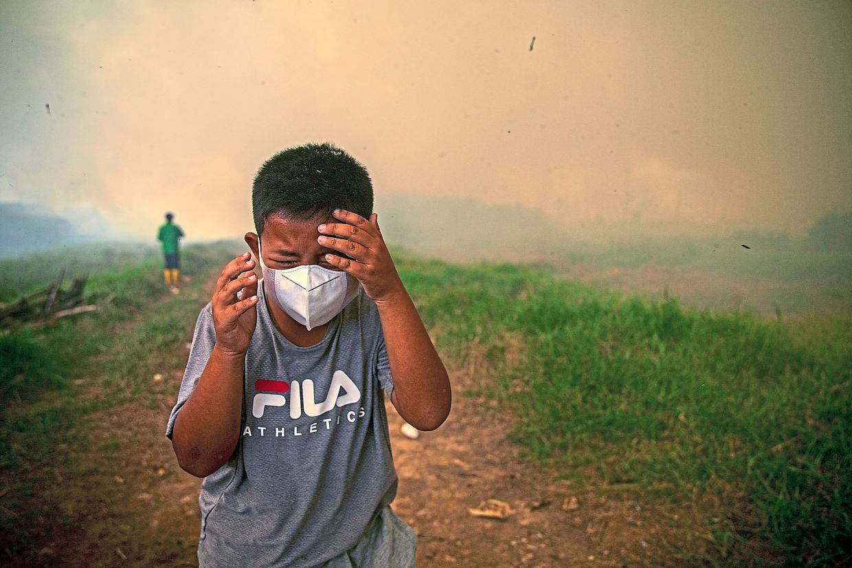 A boy reacting as thick smoke rises from wildfires near a residential area in Ogan Ilir, South Sumatra province. — Reuters