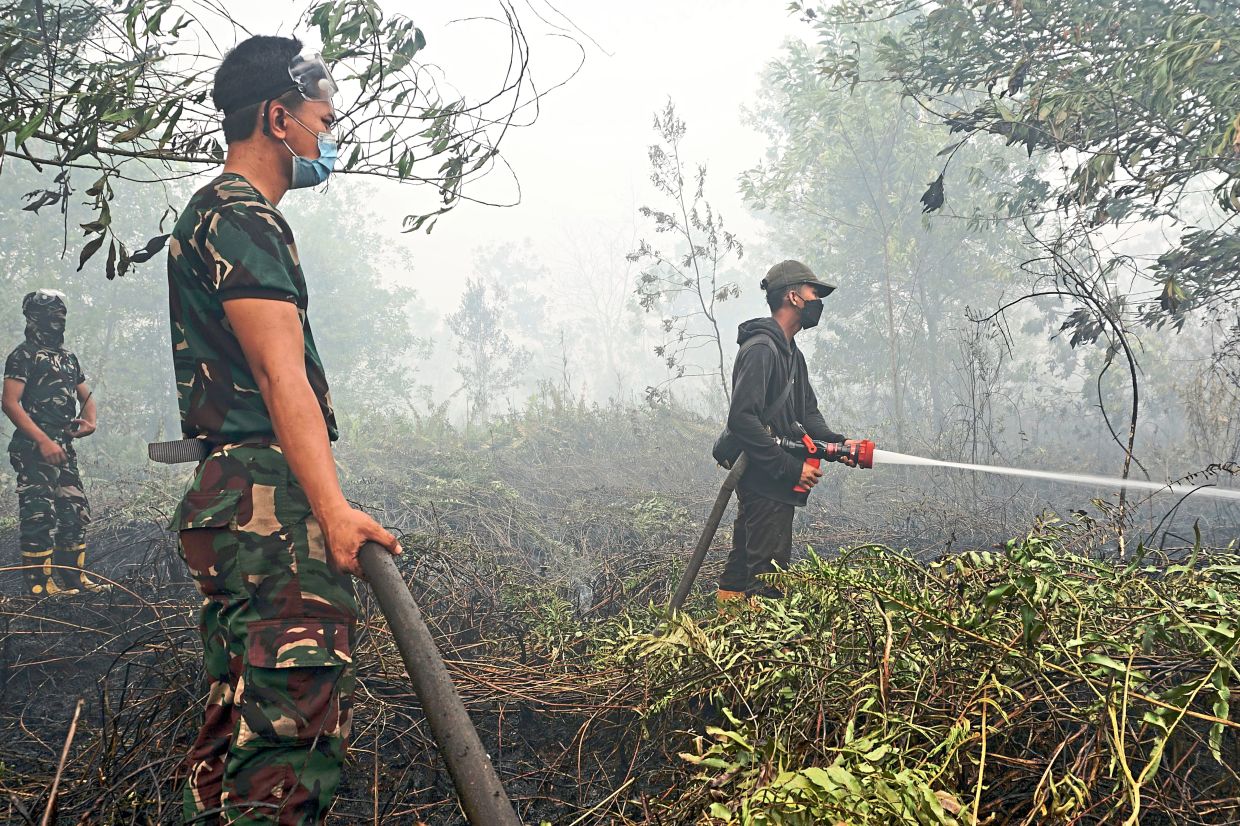 Firefighters battling a wildfire sweeping through a peatland field in Jekan Raya, Central Kalimantan, spraying water into the smoke and flames. — AP