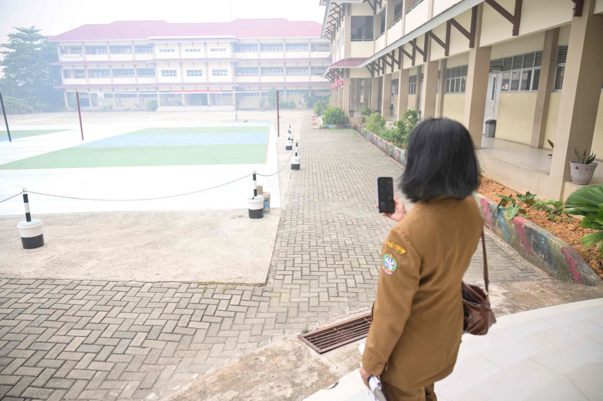 A teacher communicating with students on her phone while standing in the compound of her school seen shrouded in smog, after local authorities mandated remote learning due to haze from land and forest fires in Pontianak, West Kalimantan, on Sept 7, 2026. - AFP