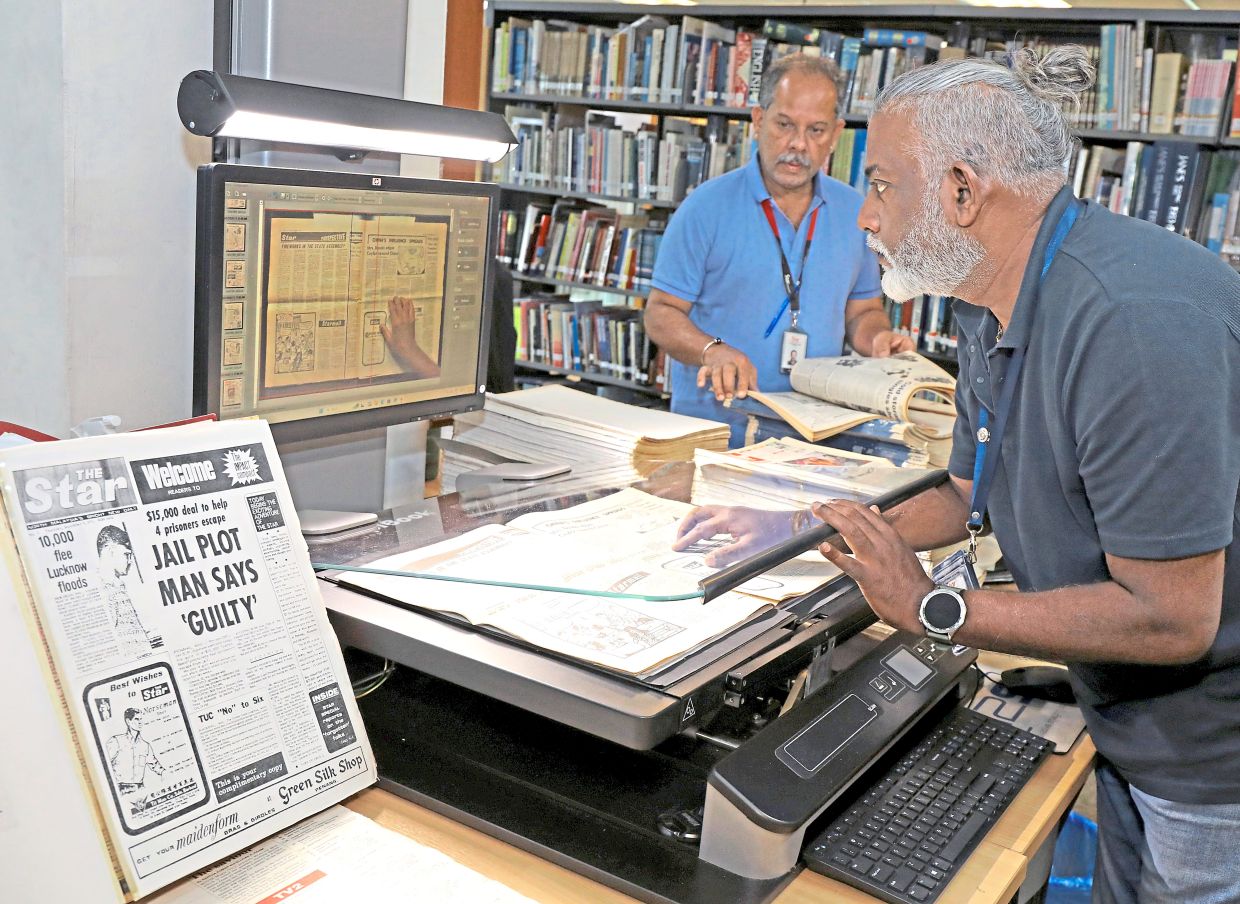Library staff member P. Nathan (right) digitising archived editions of The Star with a specialised CopiBook scanner, while Ravi checks archival material.