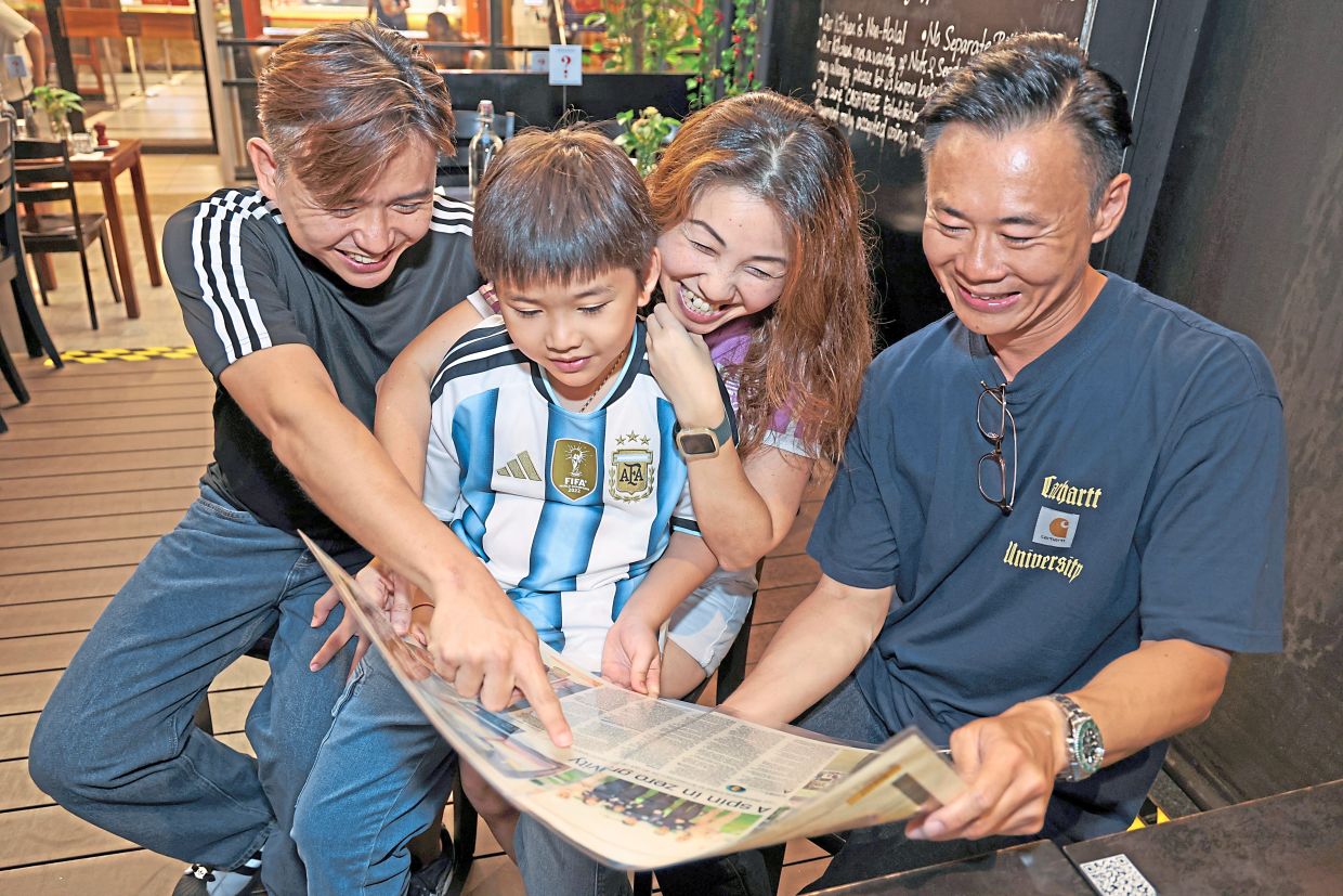 Lau, her husband Lim Kee Aun (left) and their son together with fellow Amsterdam travel companion Siau looking through an old clipping from ‘The Star’.
