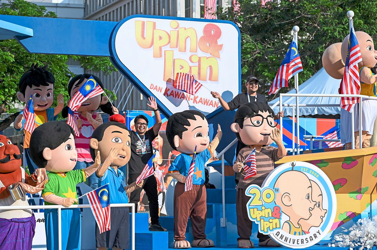 Popular animation characters Upin and Ipin wave to the crowd from a float.