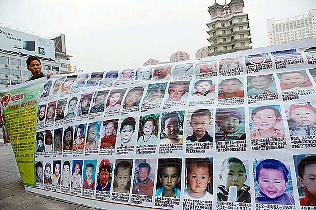 On October 12, 2010, at Zhengzhou’s Erqi Square, a parent held up a banner plastered with photos of missing children. He hoped to gather leads for his own missing child and those of 2,000 other families. - Photo: CYOL.net