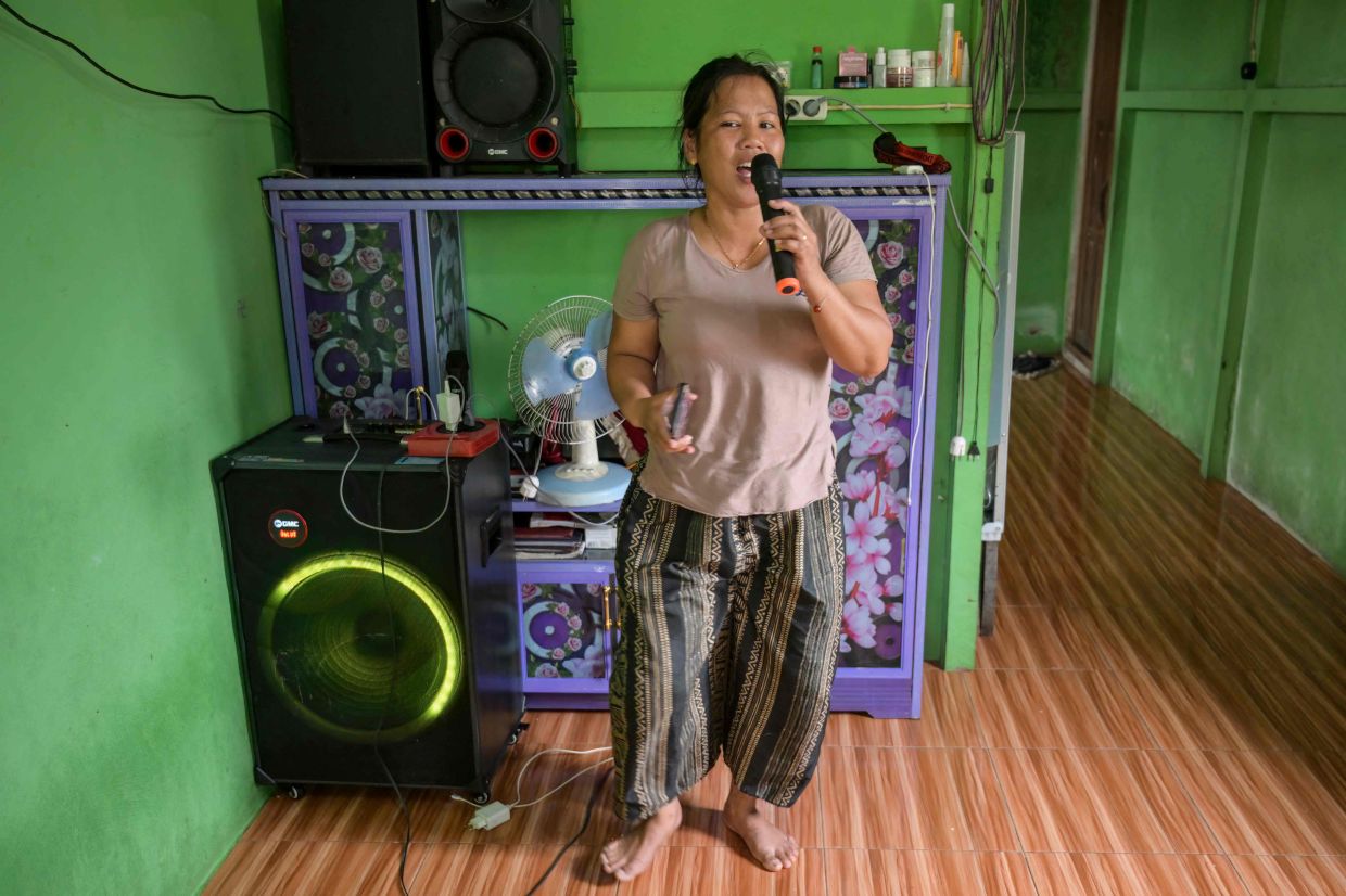 This picture taken on September 2, 2026 shows Borneo Future Indonesia wildlife observer Katarina Siti singing using a karaoke machine she bought with the money earned from observing wildlife in Sungai Ajung village in Kapuas Hulu, West Kalimantan. Indonesian villager Octavius wades through the forest in rubber boots and tattered joggers, ears pricked, eyes peeled, a telephoto lens on his phone primed to capture orangutans, monkeys or birds. The daily photo hunt earns Octavius and hundreds of others in Borneo cash as part of a conservation programme seeking to make animals worth more alive than dead. (Photo by BAY ISMOYO / AFP) / To go with 'INDONESIA-ENVIRONMENT-CONSERVATION-ANIMAL,FOCUS' by Mariette le ROUX
