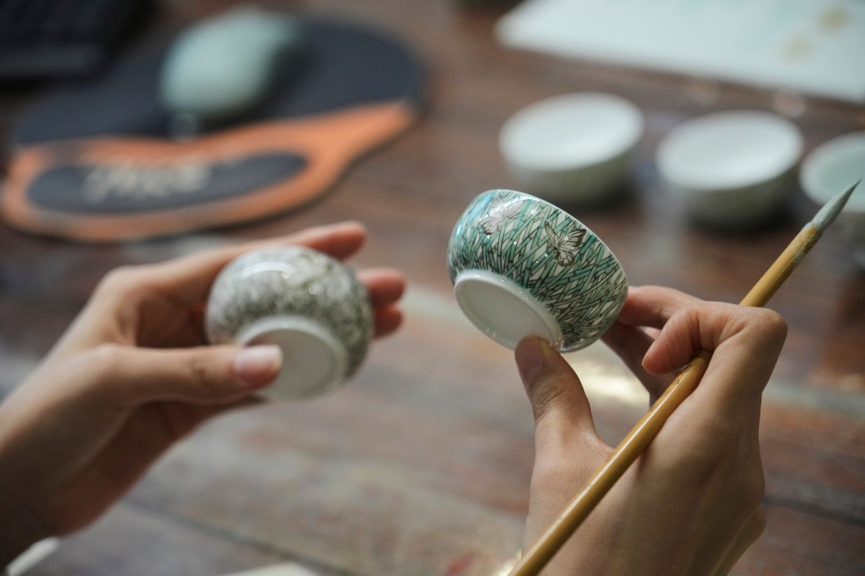 Chinese porcelain artist Chen Qing holds up two cups after painting them in Jingdezhen.