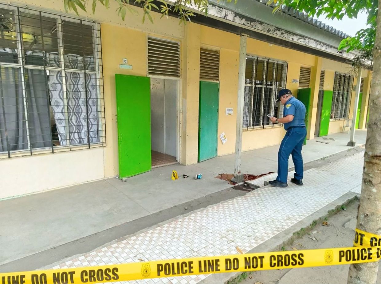 A police investigator stands next to a pool of blood after a shooting incident at a classroom entrance in a high school in Banga town, South Cotabato, in southern island of Mindanao on September 18, 2026. A student killed at least two people at a school in the southern Philippines on Friday before turning the gun on himself, officials told AFP, the country's third deadly campus attack since June. -- Photo by AFP