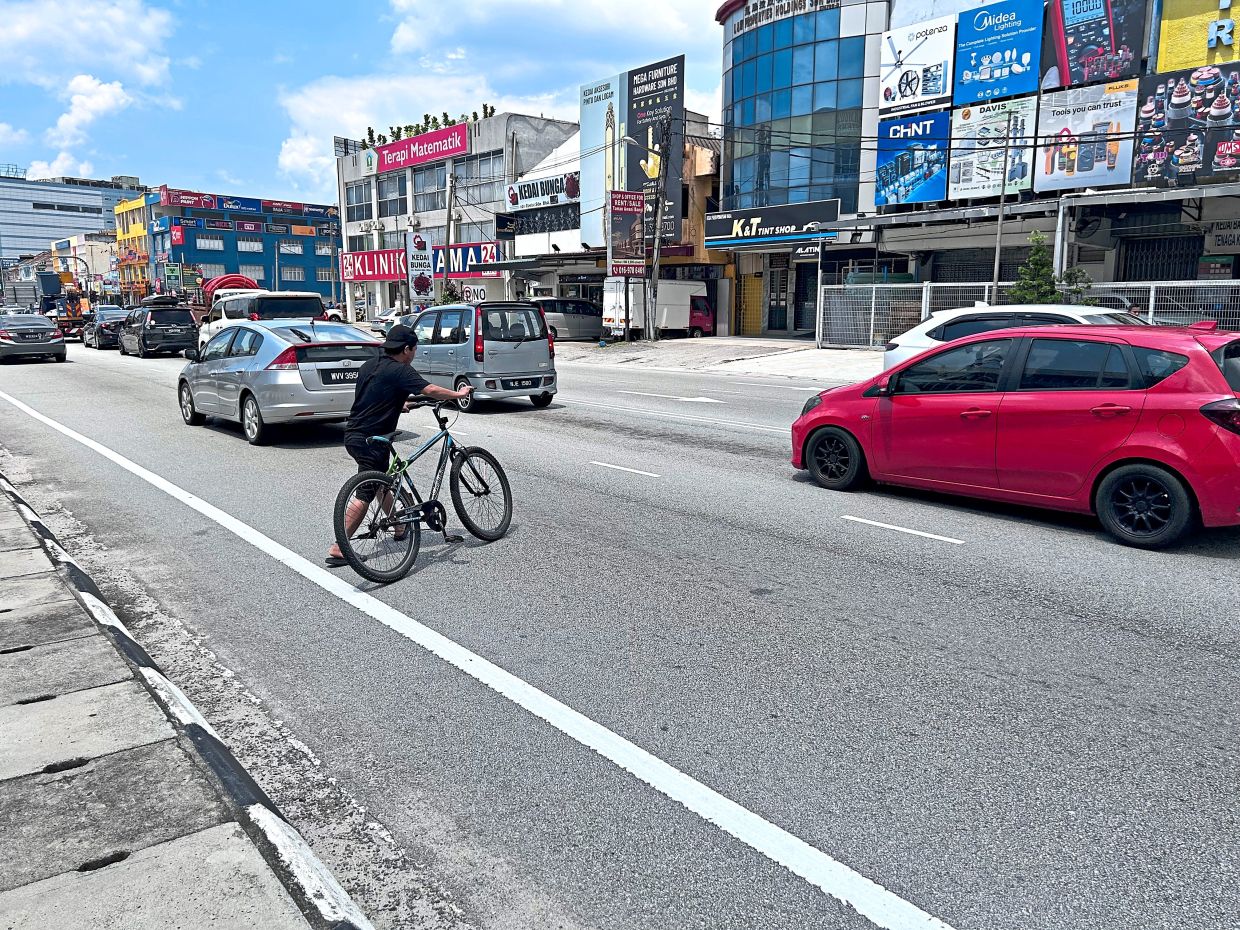 A man pushes his bicycle across the street among cars along Jalan Sungai Chua, Kajang.