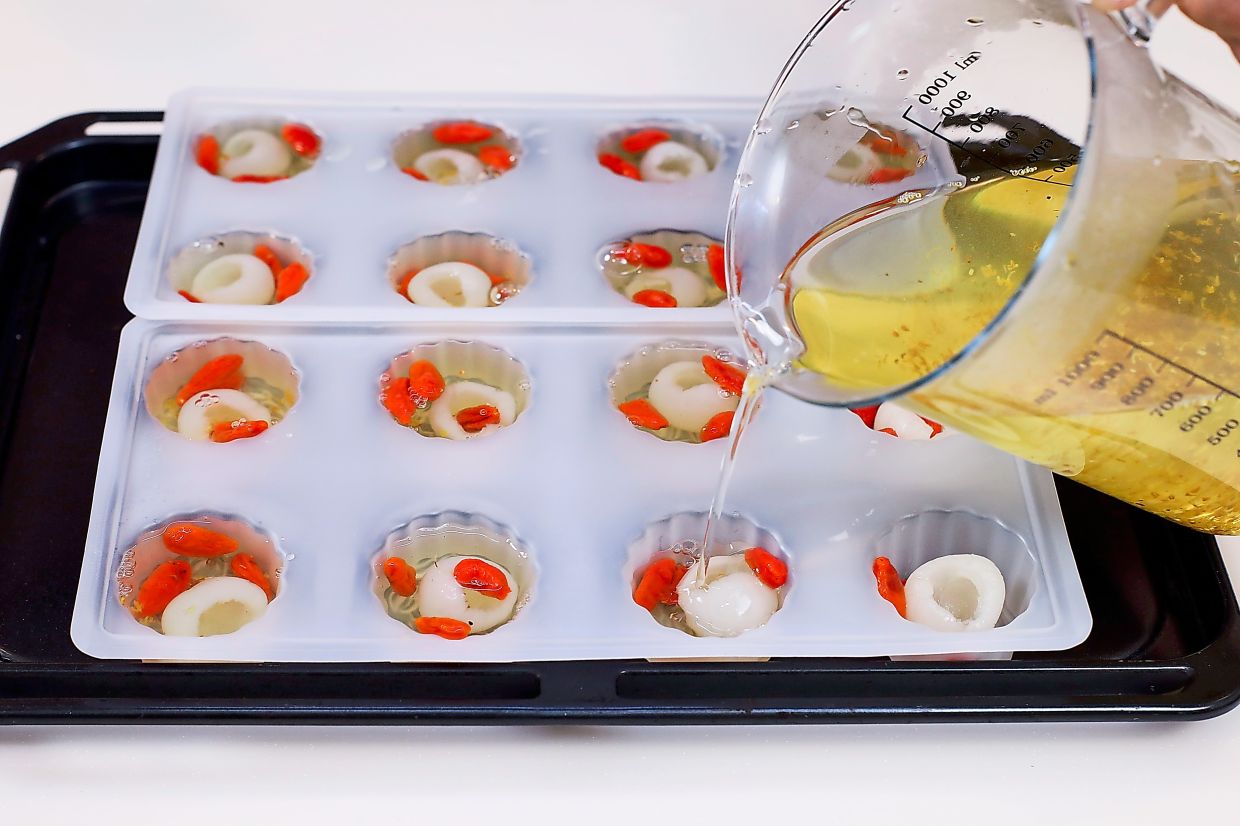 Fill each mould cavity with a piece of longan, three pieces of wolfberries, and topped with the lukewarm osmanthus jelly mixture.
