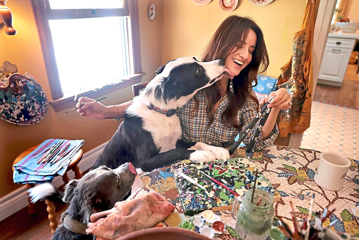 Saleh gets a surprise kiss from her dog Olive while painting candles at her dining room table.