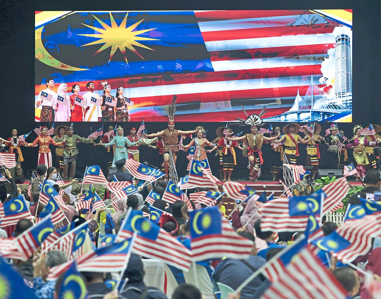 A cultural performance at Dewan Milenium in Kepala Batas during a state-level Malaysia Day celebration, with the waving crowd displaying a sea of mini Jalur Gemilang.