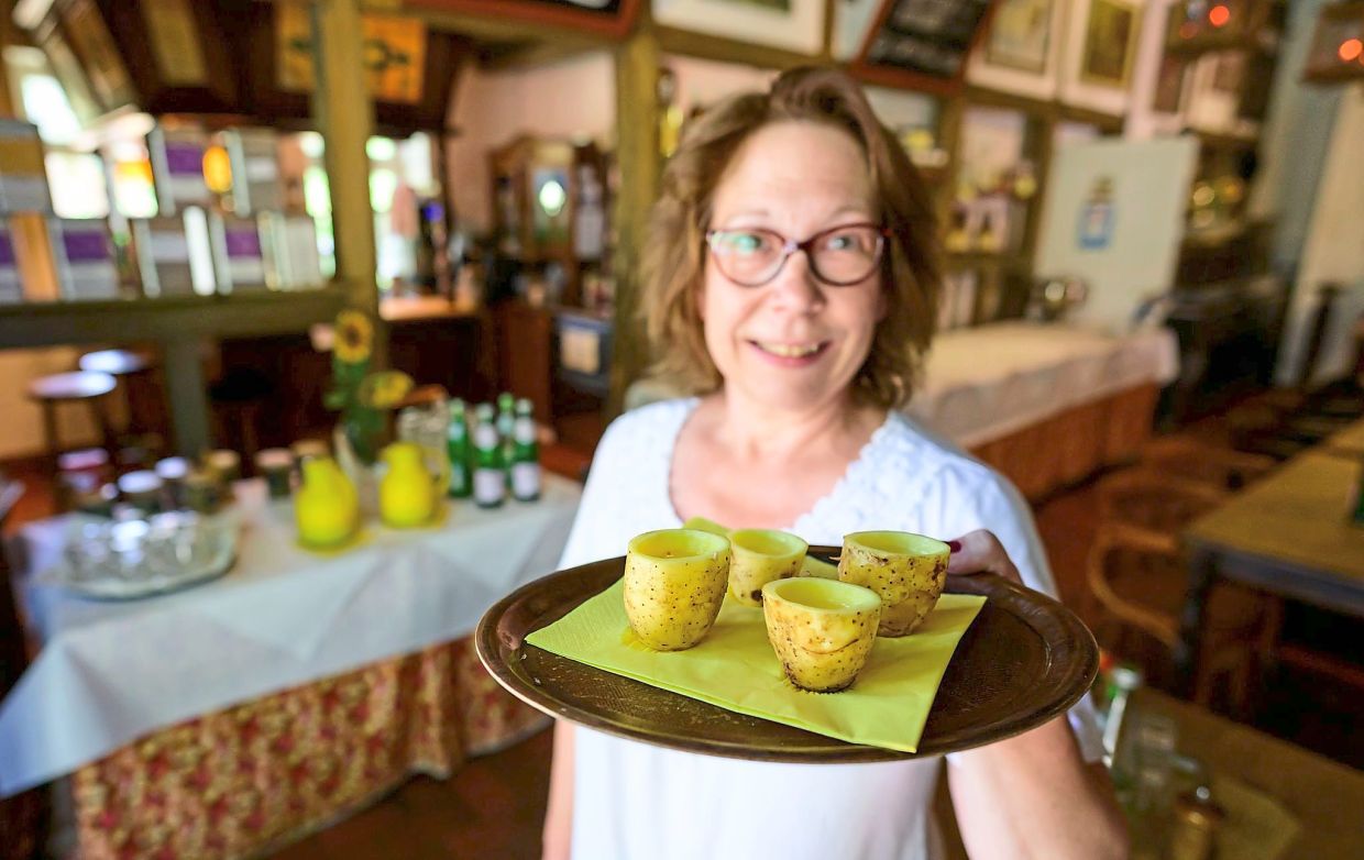 Ilka Frohlich, who works at the hotel, offering potato schnaps served in tumblers made of spuds, while Brohzat is applying a face mask made of spuds on a guest at the hotel. 