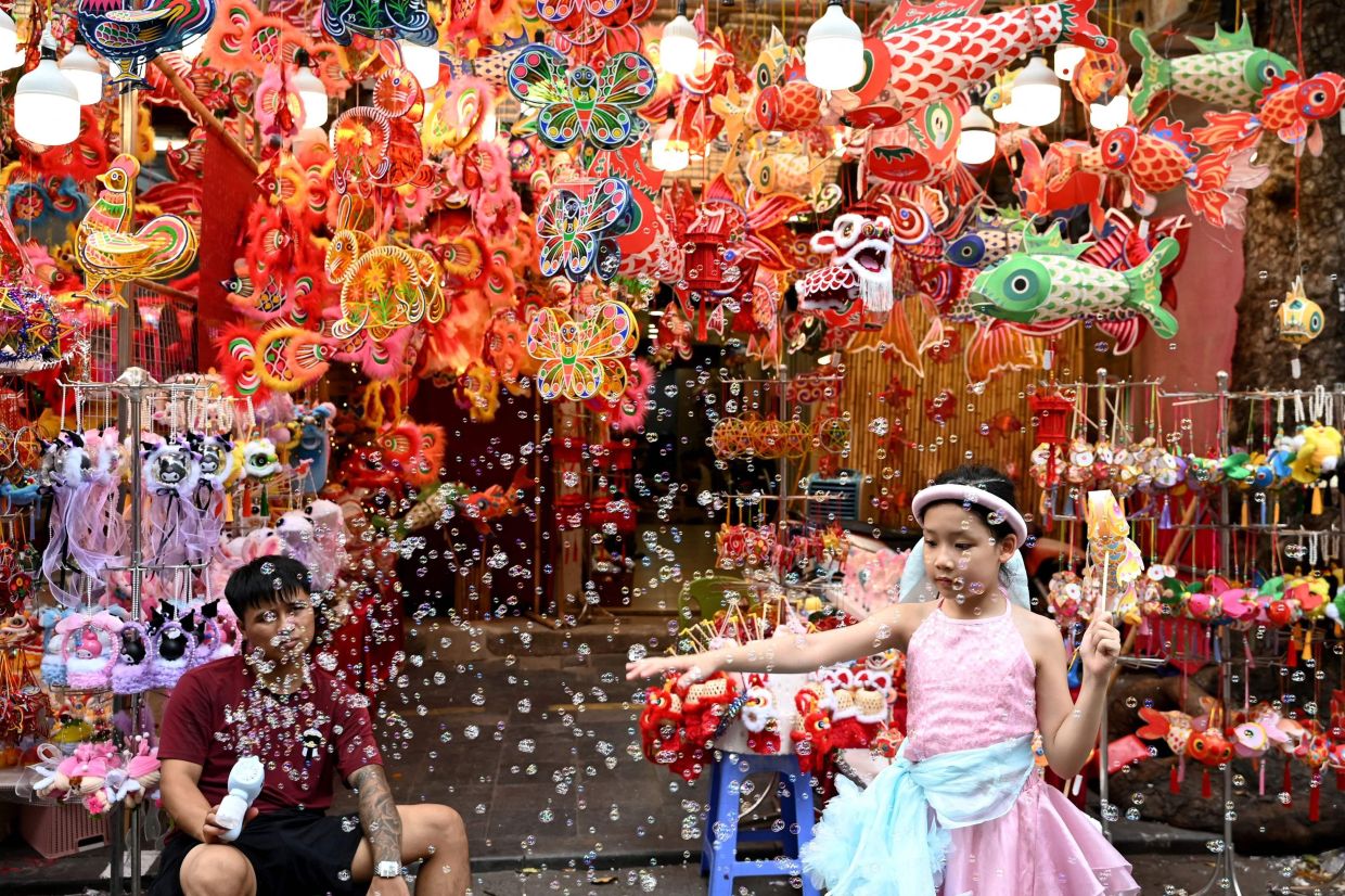 A young girl plays with bubbles in front of a toy stall selling items ahead of the Mid-Autumn Festival in Hanoi's old quarters on Monday, September 21, 2026. (Photo by Nhac NGUYEN / AFP)